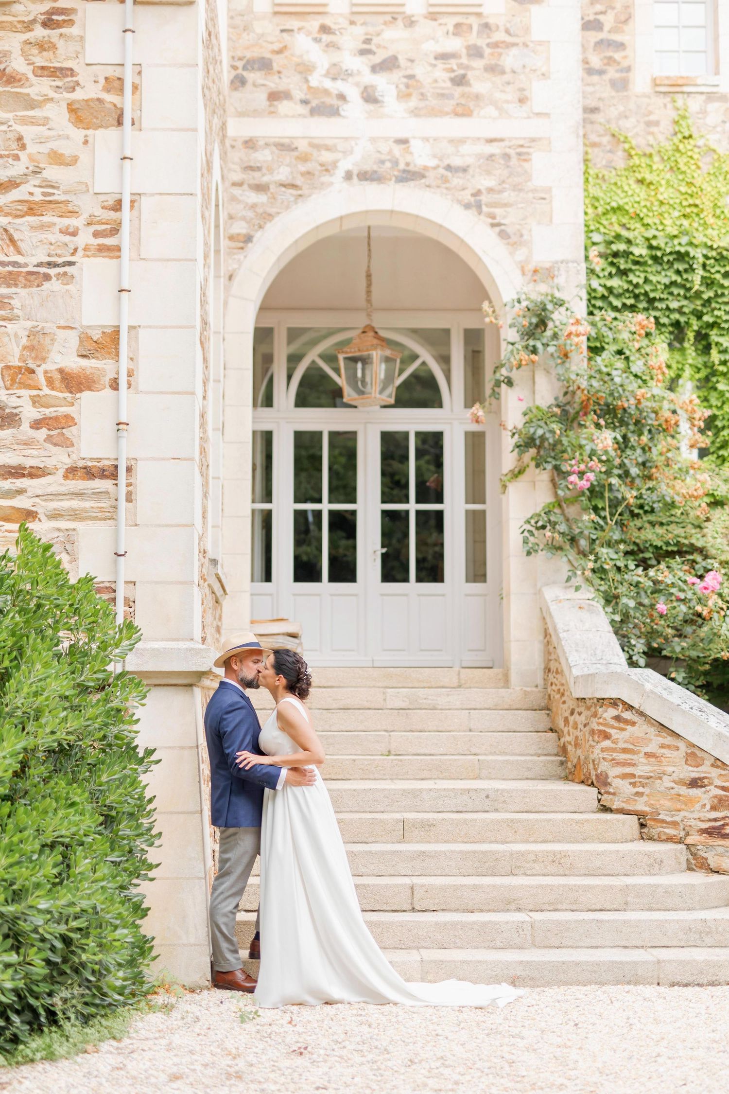 A wedding couple shares intimate moments on the steps of a rustic stone building with white trim.