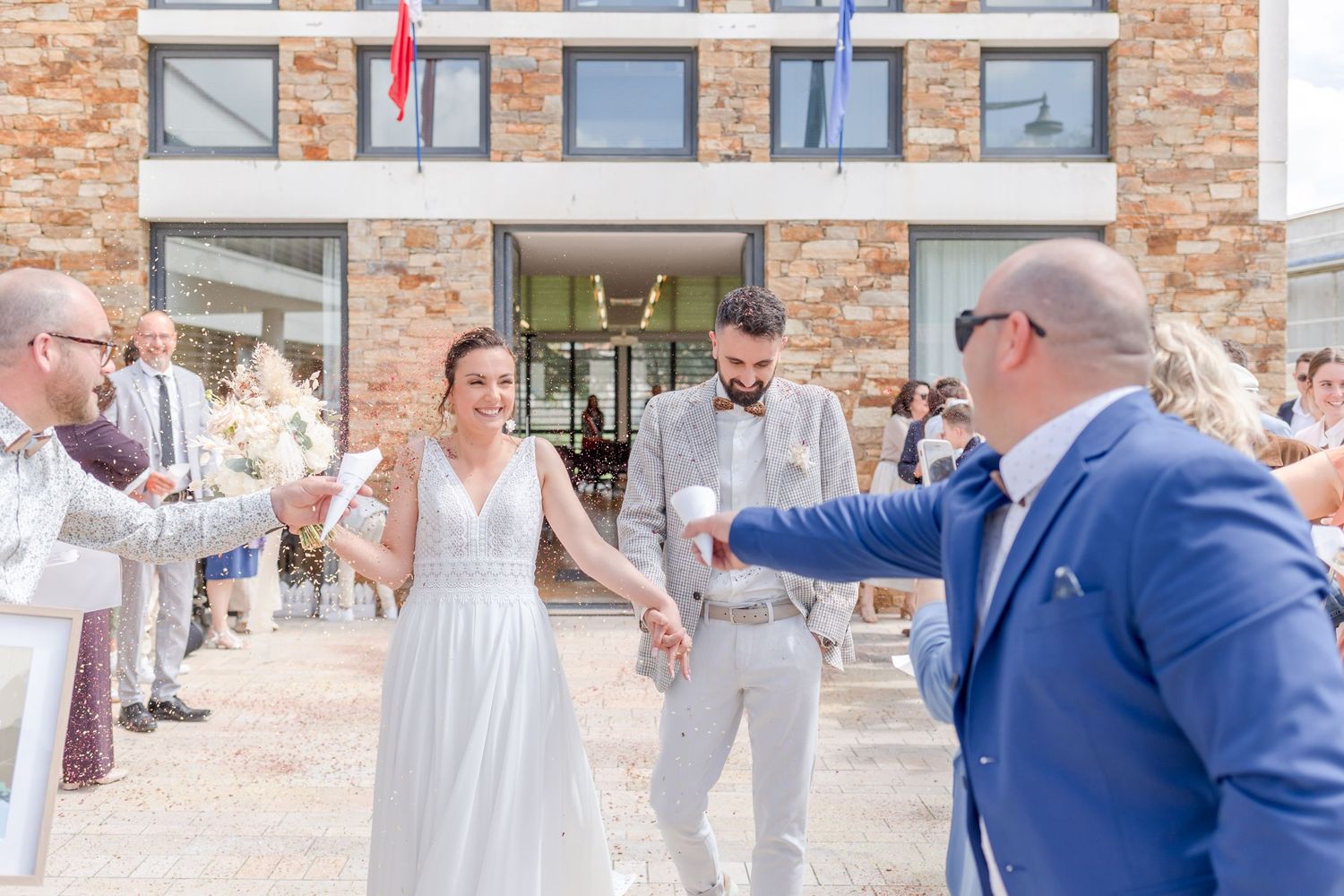 Newlyweds celebrate with guests outside a brick building on their wedding day.