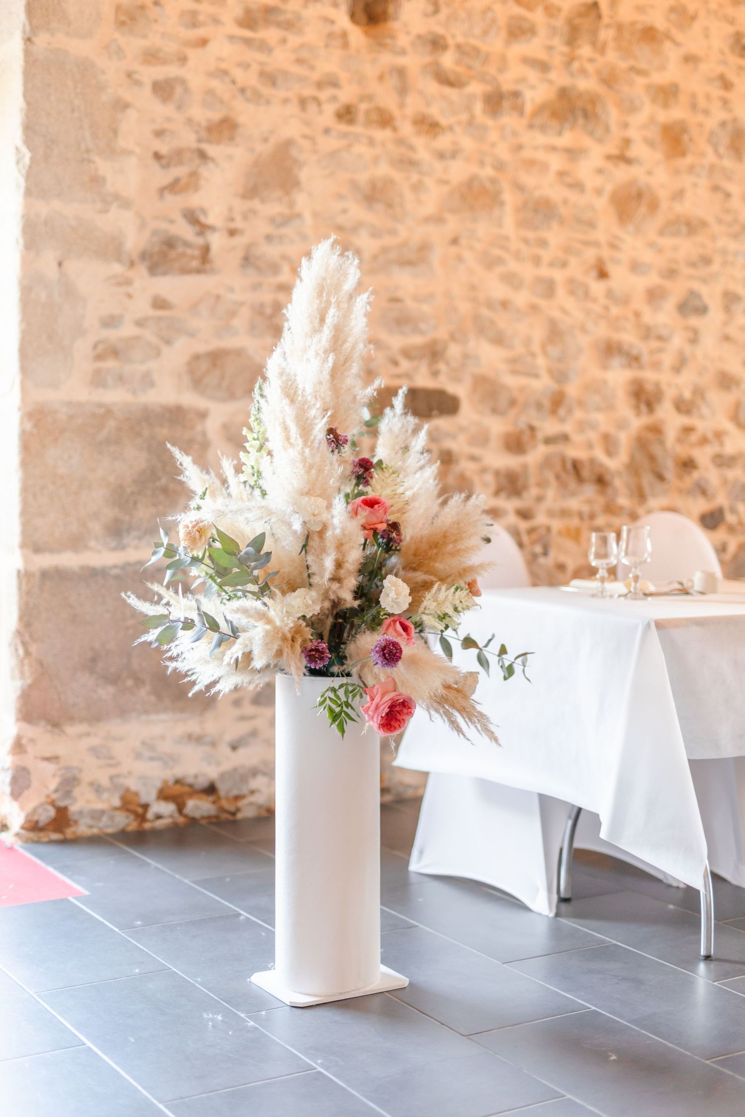 White floral arrangements with pampas grass displayed against a stone wall.