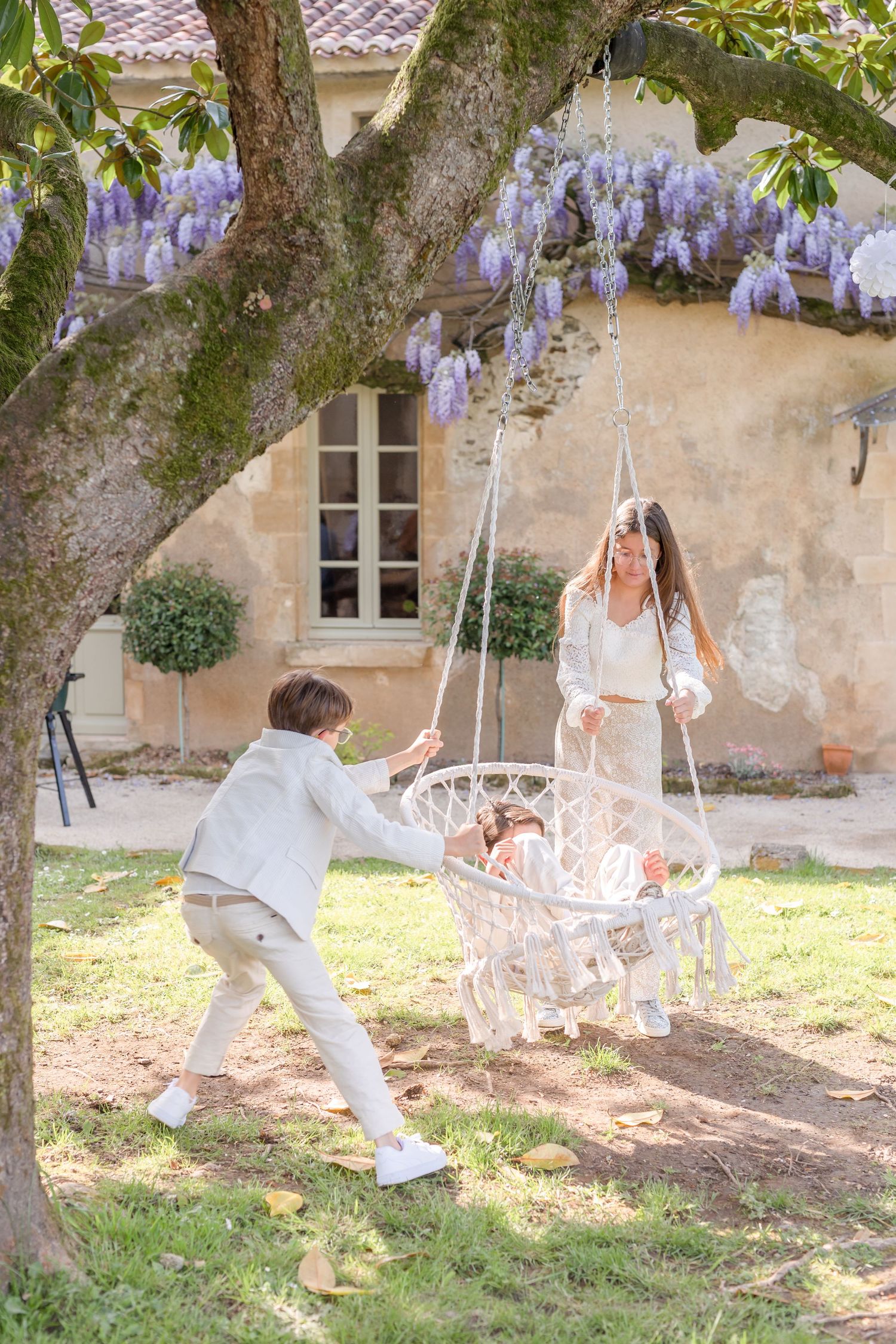White hammock swinging in a garden with wisteria and stone walls.