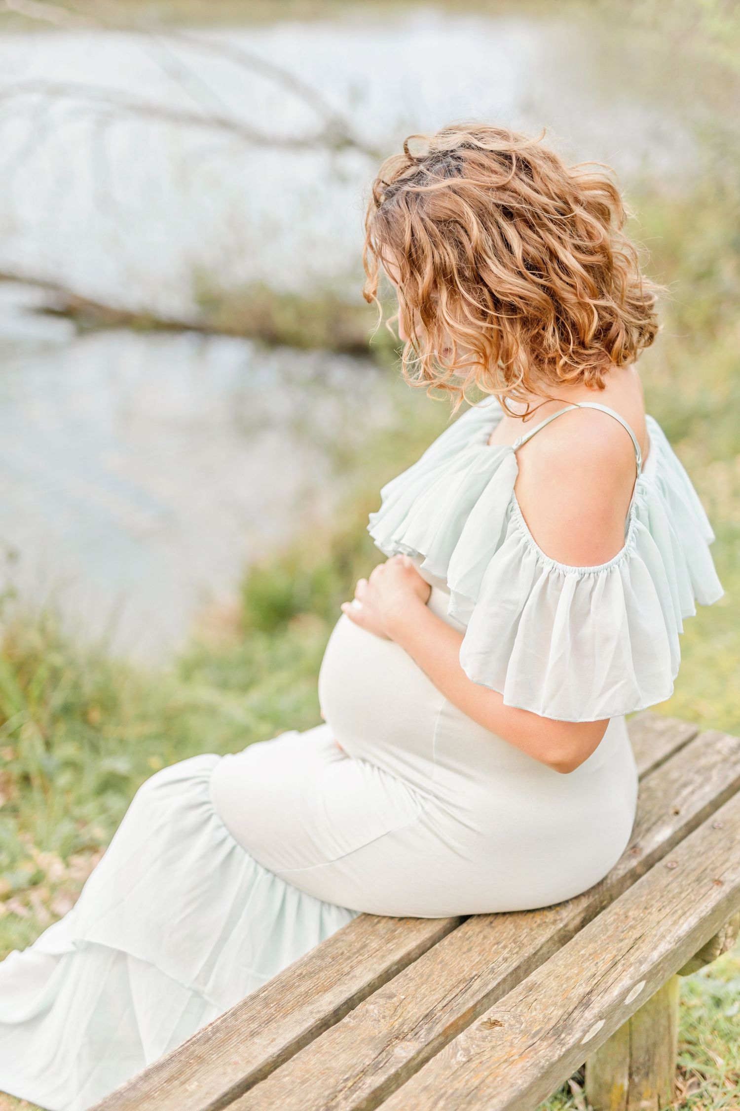 Peaceful maternity portrait on rustic wooden bench by the water's edge.