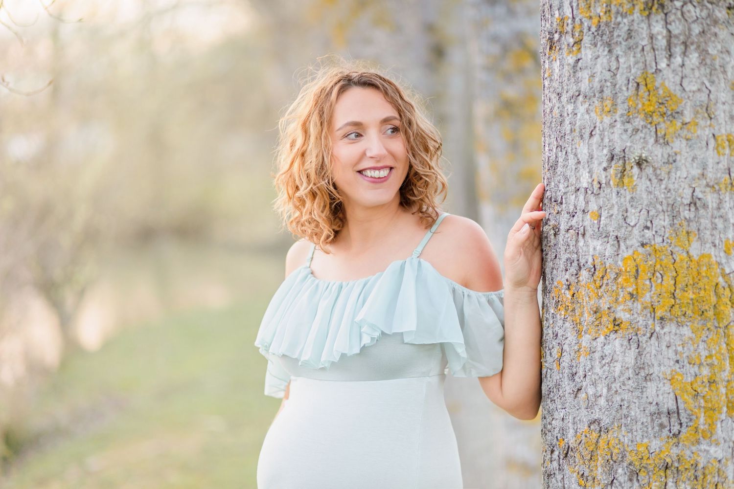 Joyful outdoor maternity portrait beside a birch tree in a pale blue dress.