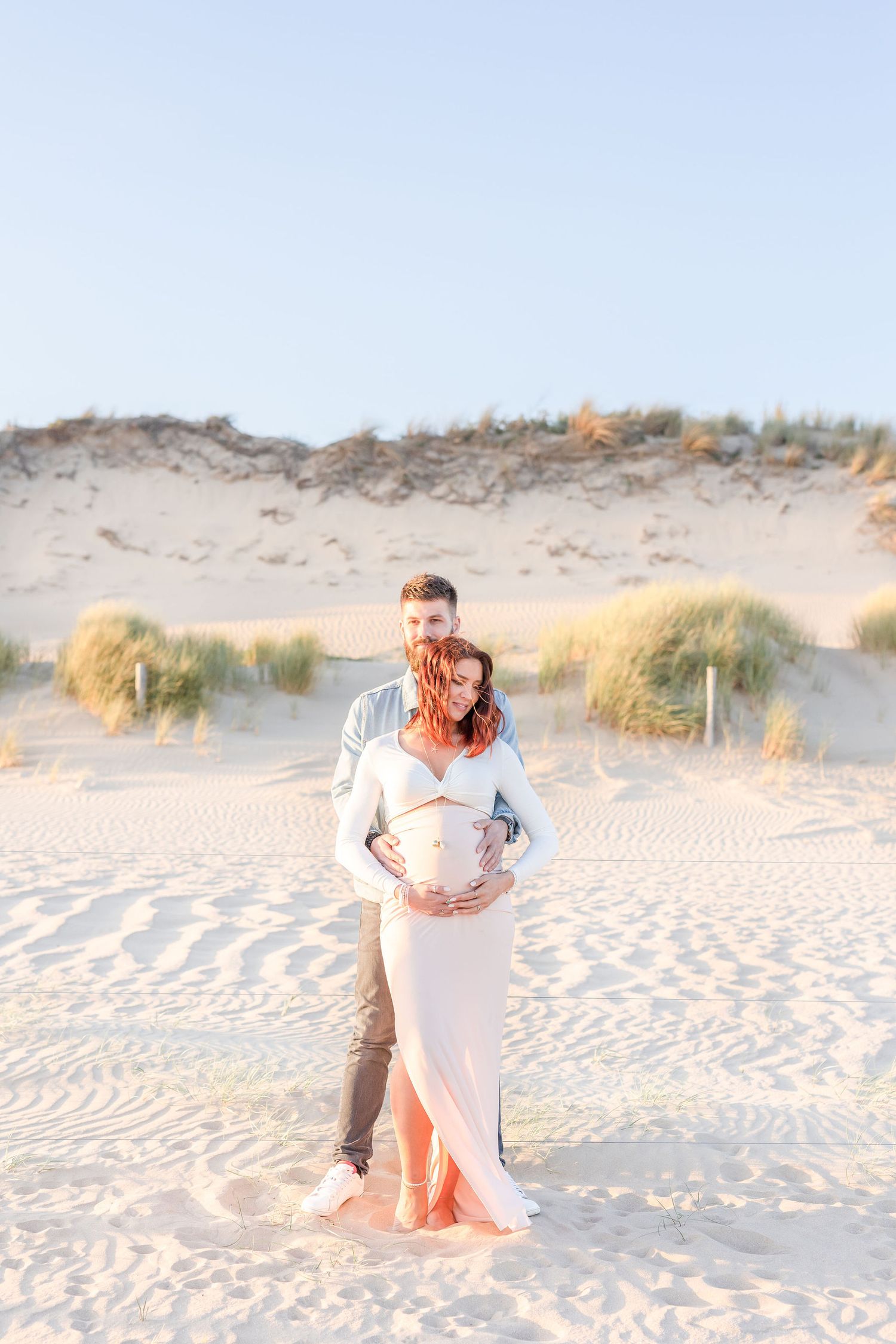 Romantic couple poses on sand dunes during golden hour beach photoshoot.