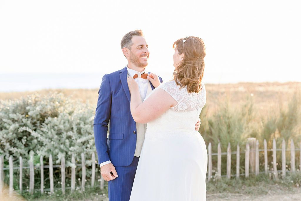 A sunny wedding portrait with a couple laughing together by coastal fencing.