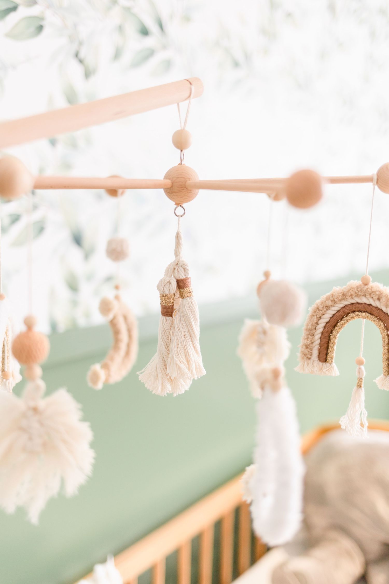 Boho nursery mobile with wooden beads, tassels, and rainbow decorations in soft peach tones.