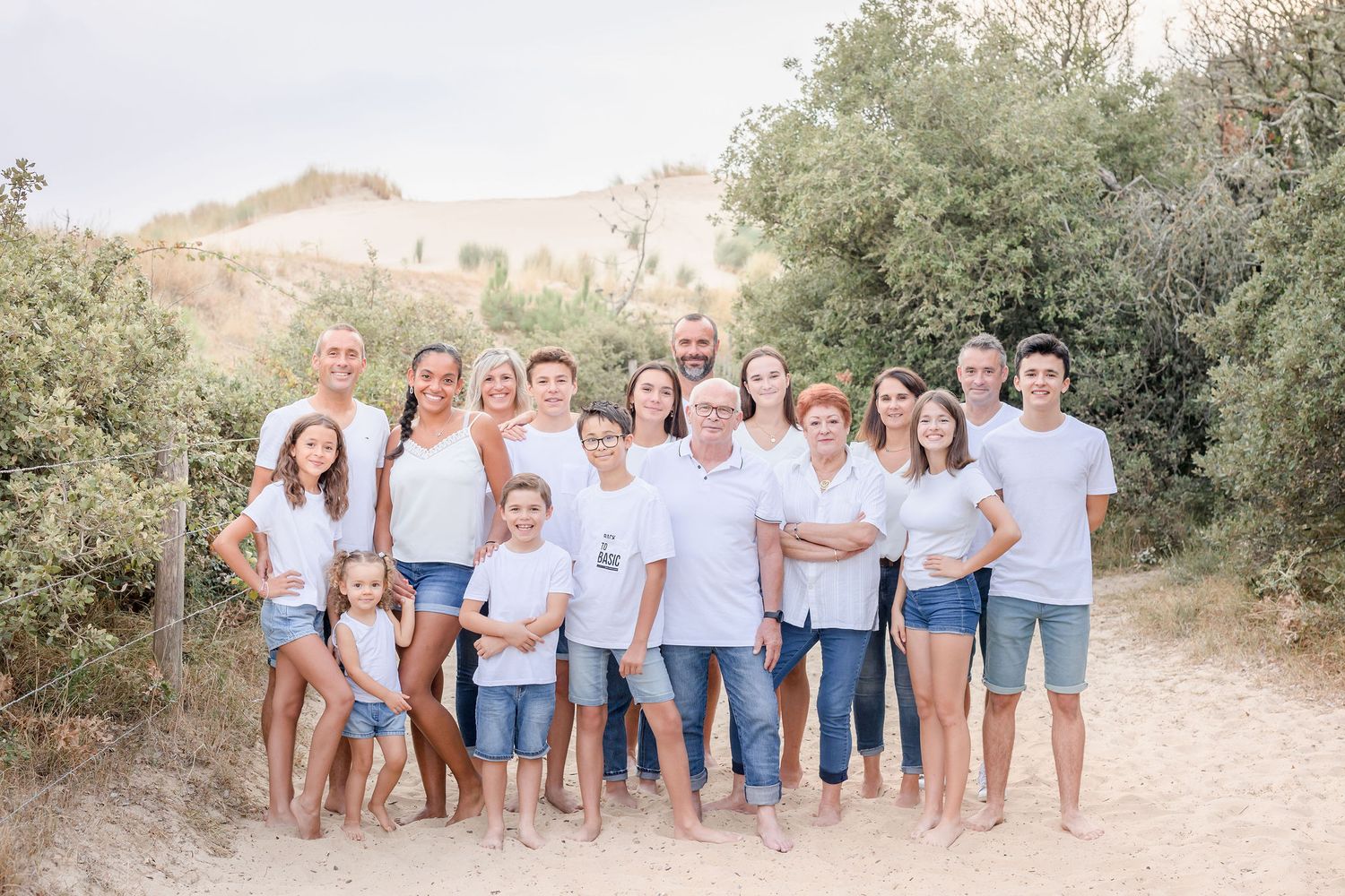 Large family group in coordinated white and denim outfits poses on sandy path.