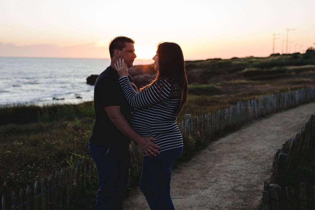 Silhouetted couple embracing during sunset maternity session by the ocean.