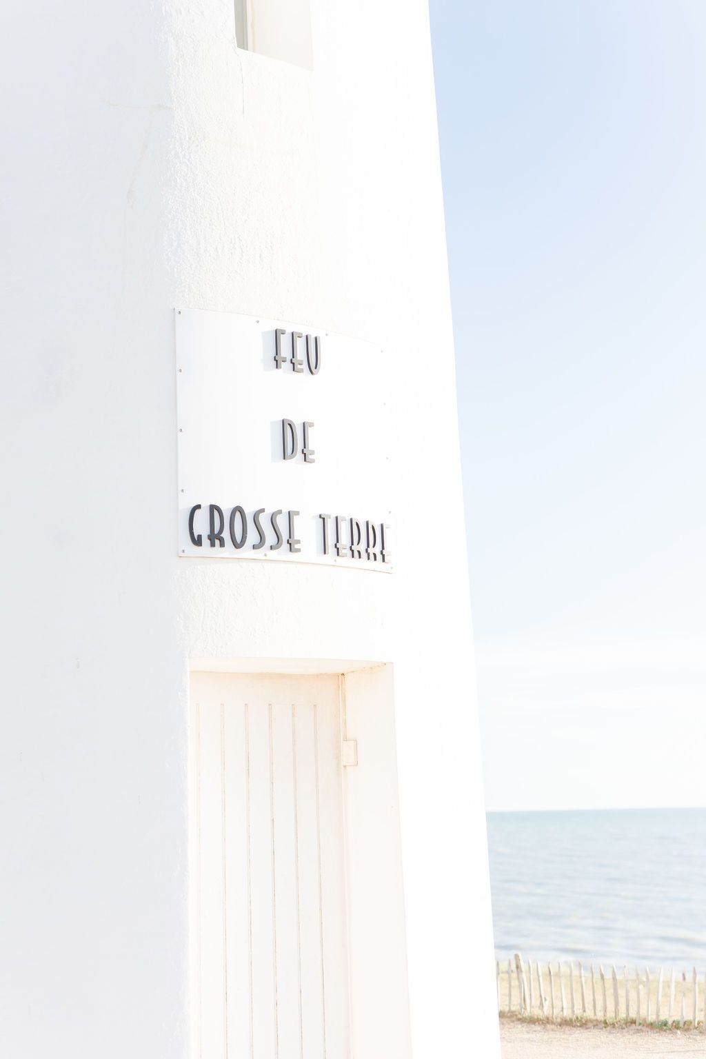 Close-up of white lighthouse with text 'Grosse Terre' against blue sky.