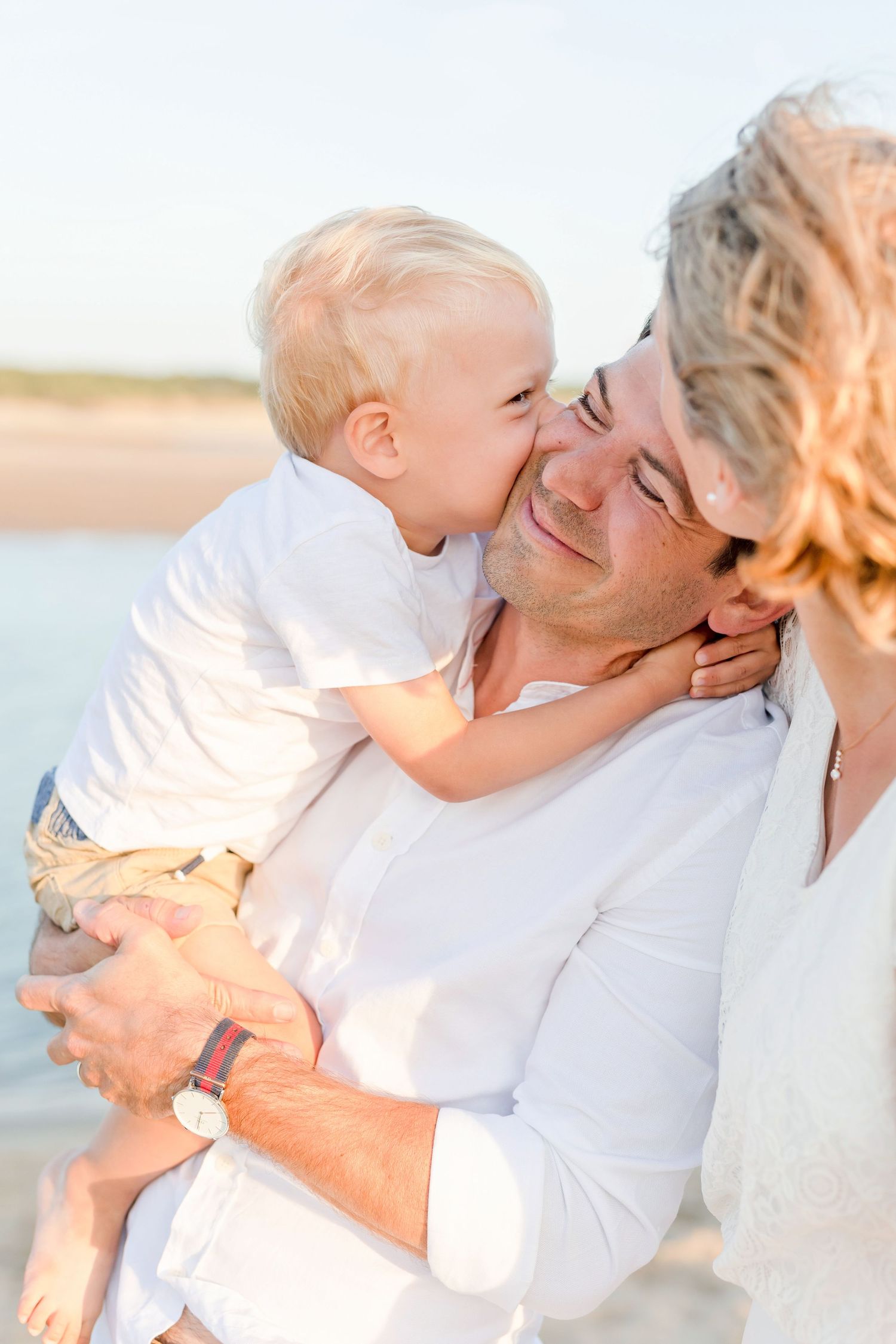 Sweet family moment captured in soft white tones during beach photoshoot.