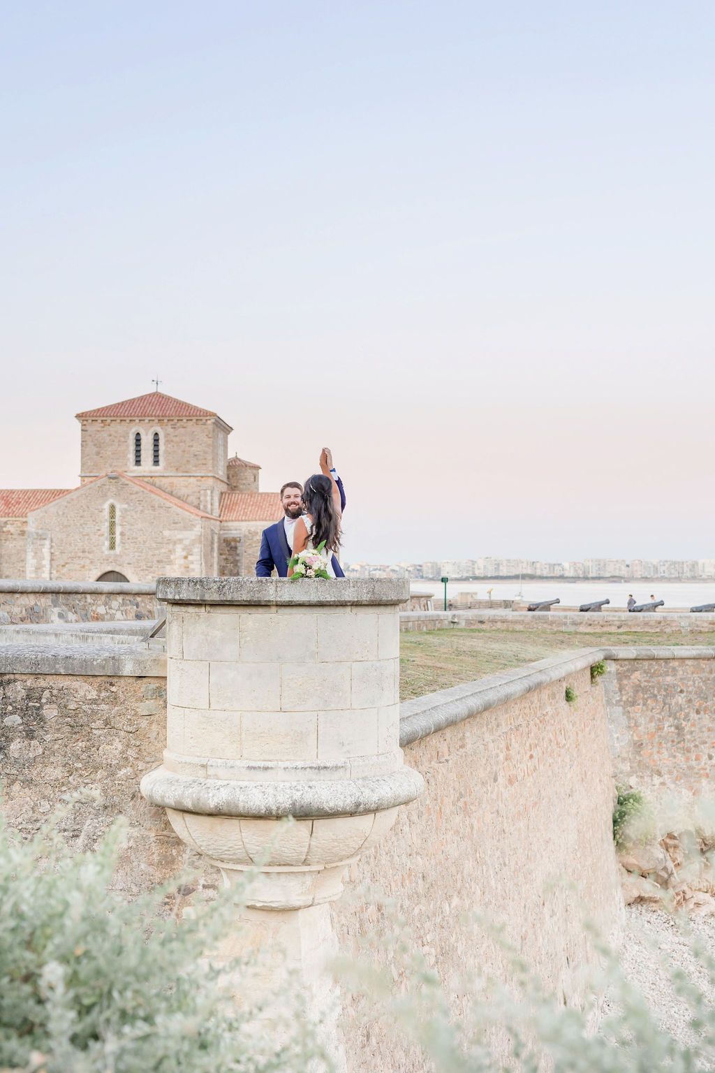 Romantic portrait session on historic stone fortification with church and sea views.