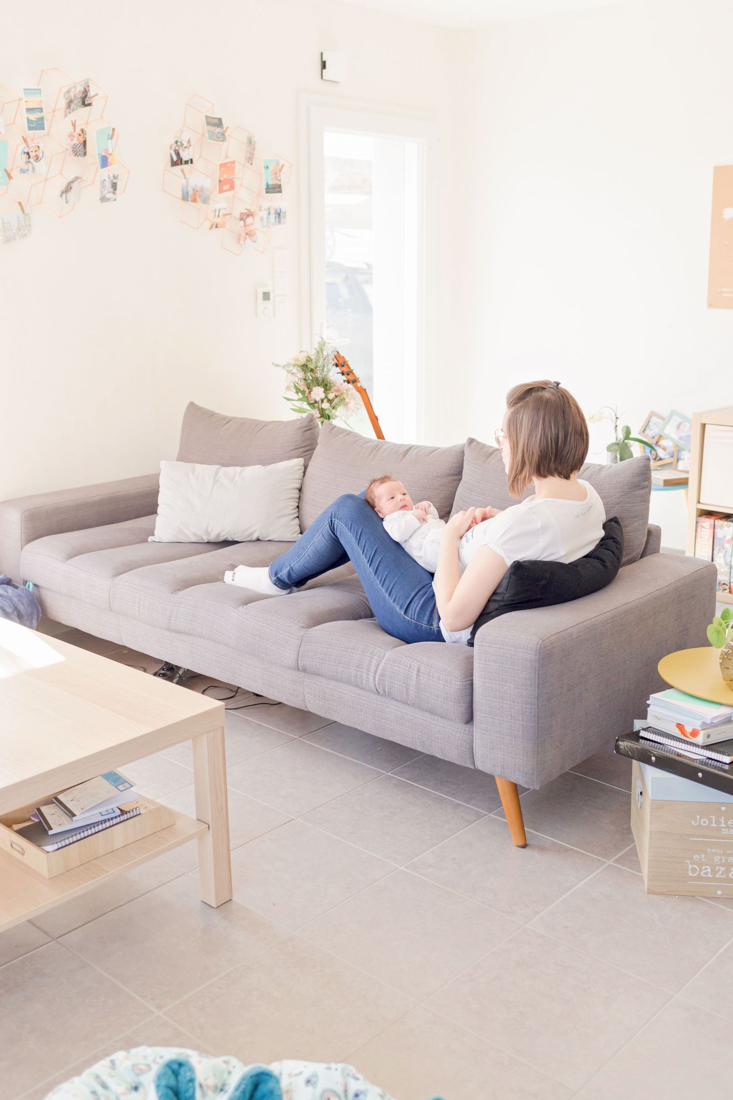 Modern living room with grey sofa and photos displayed on wall in bright natural light.