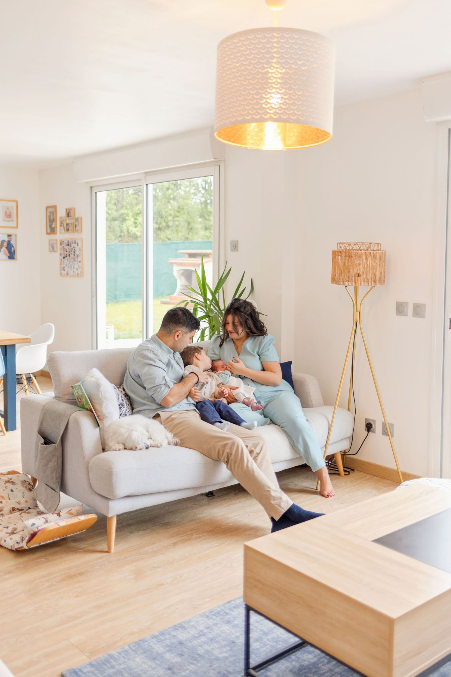 Family bonding with newborn on gray sofa in modern living room with natural lighting.