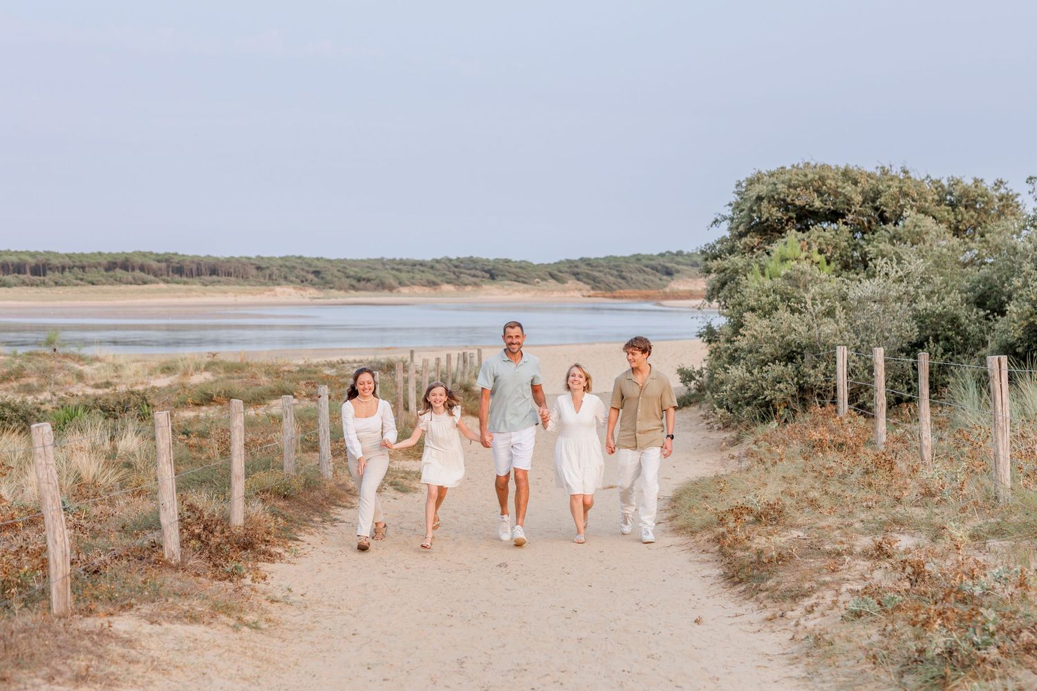Family walking together on coastal path wearing coordinated white and beige outfits.