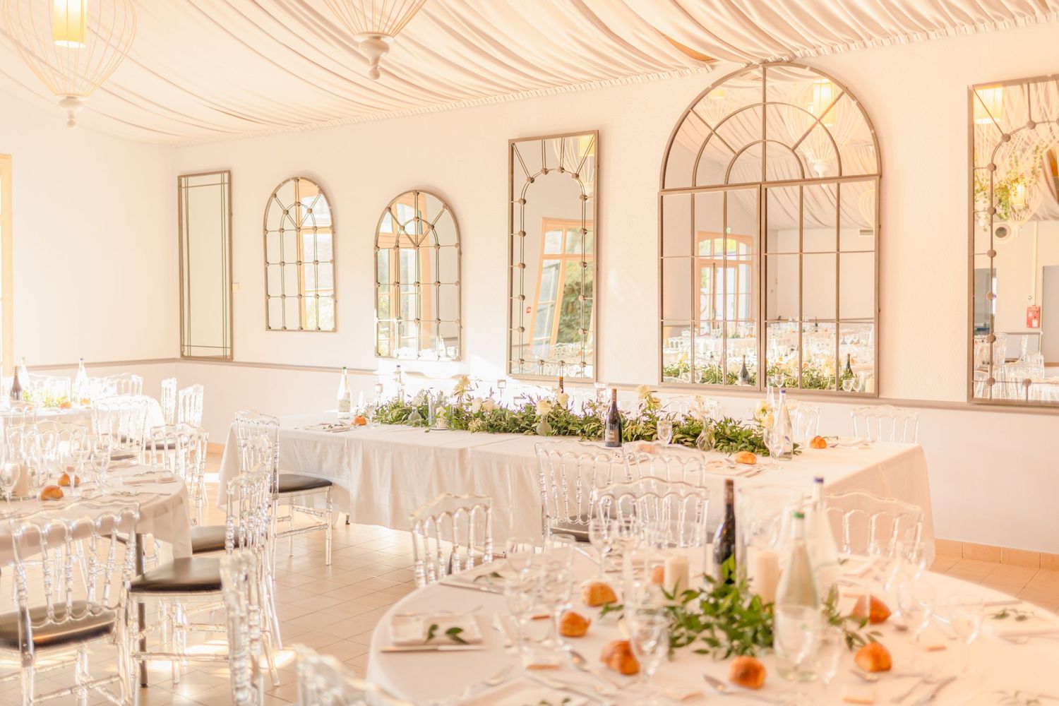 Elegant white wedding reception venue with arched windows and draped ceiling.