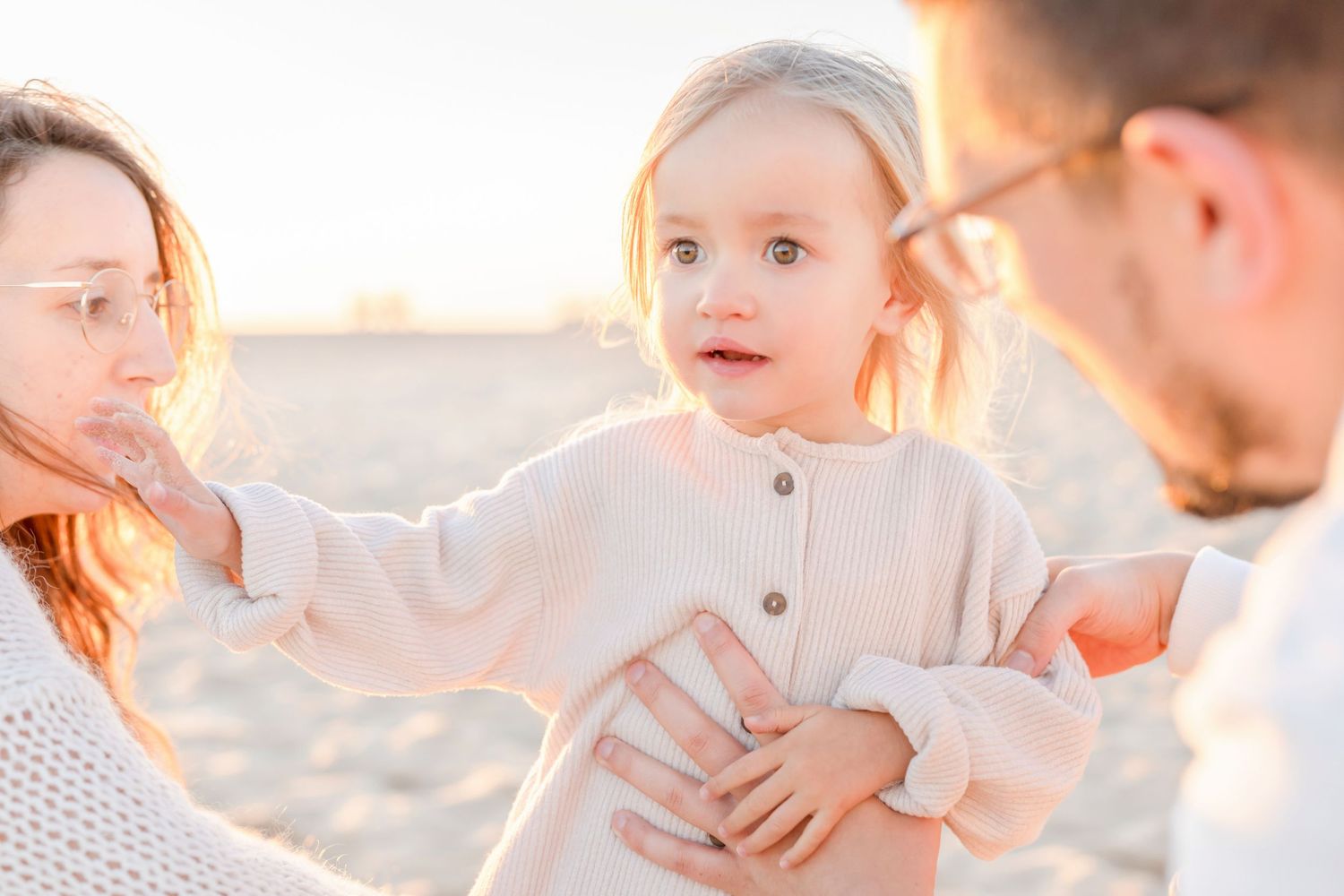 A family shares a tender moment together on a sandy beach at sunset.