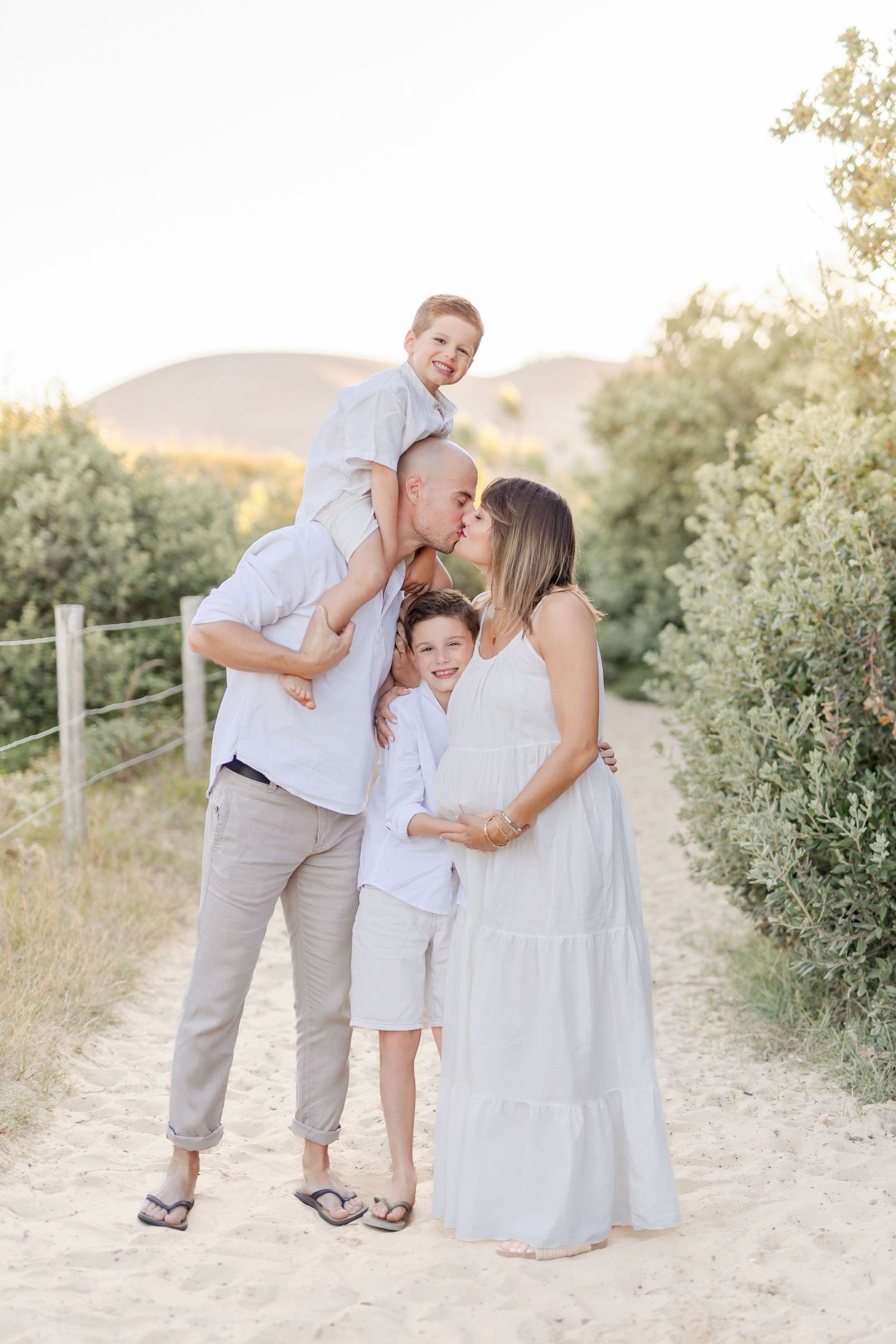 Intimate family moment shared on sandy path surrounded by coastal vegetation.