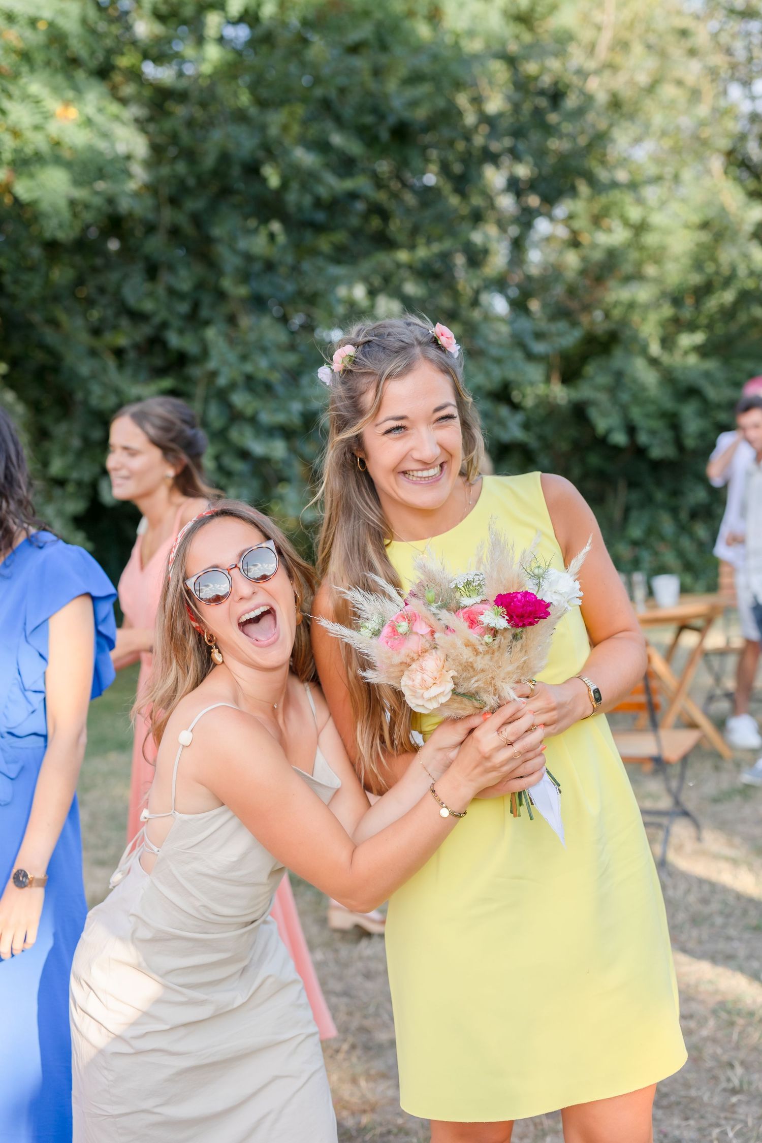 Wedding party members share laughs while holding drinks at outdoor reception.