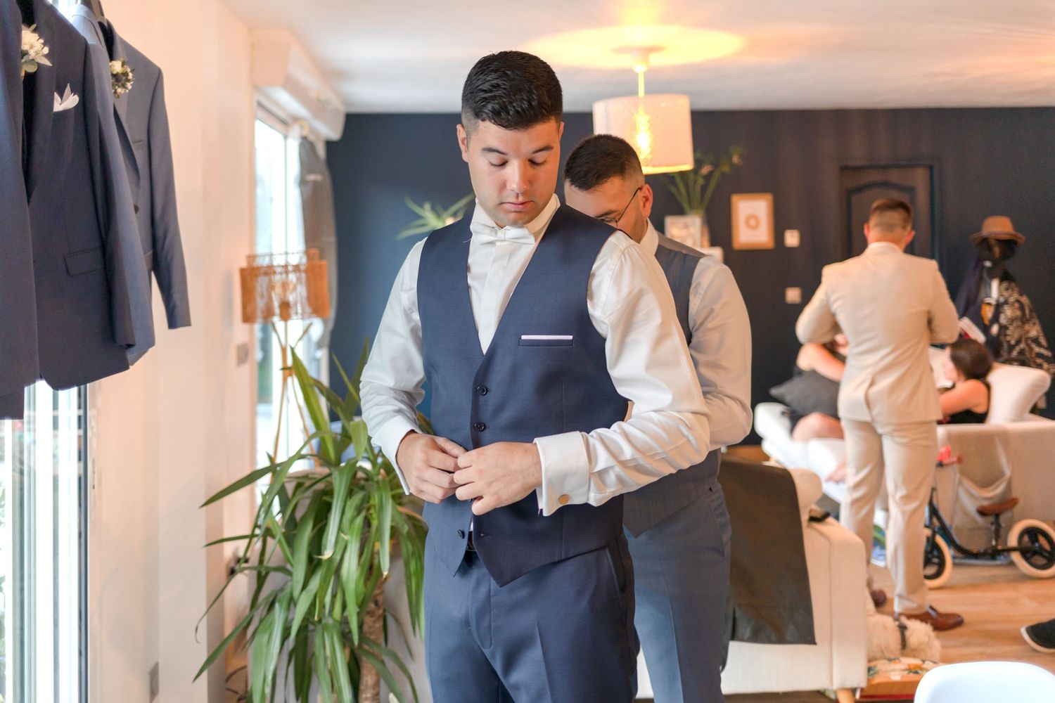 Groomsmen getting ready in a modern room with suits hanging and indoor plants as decor.