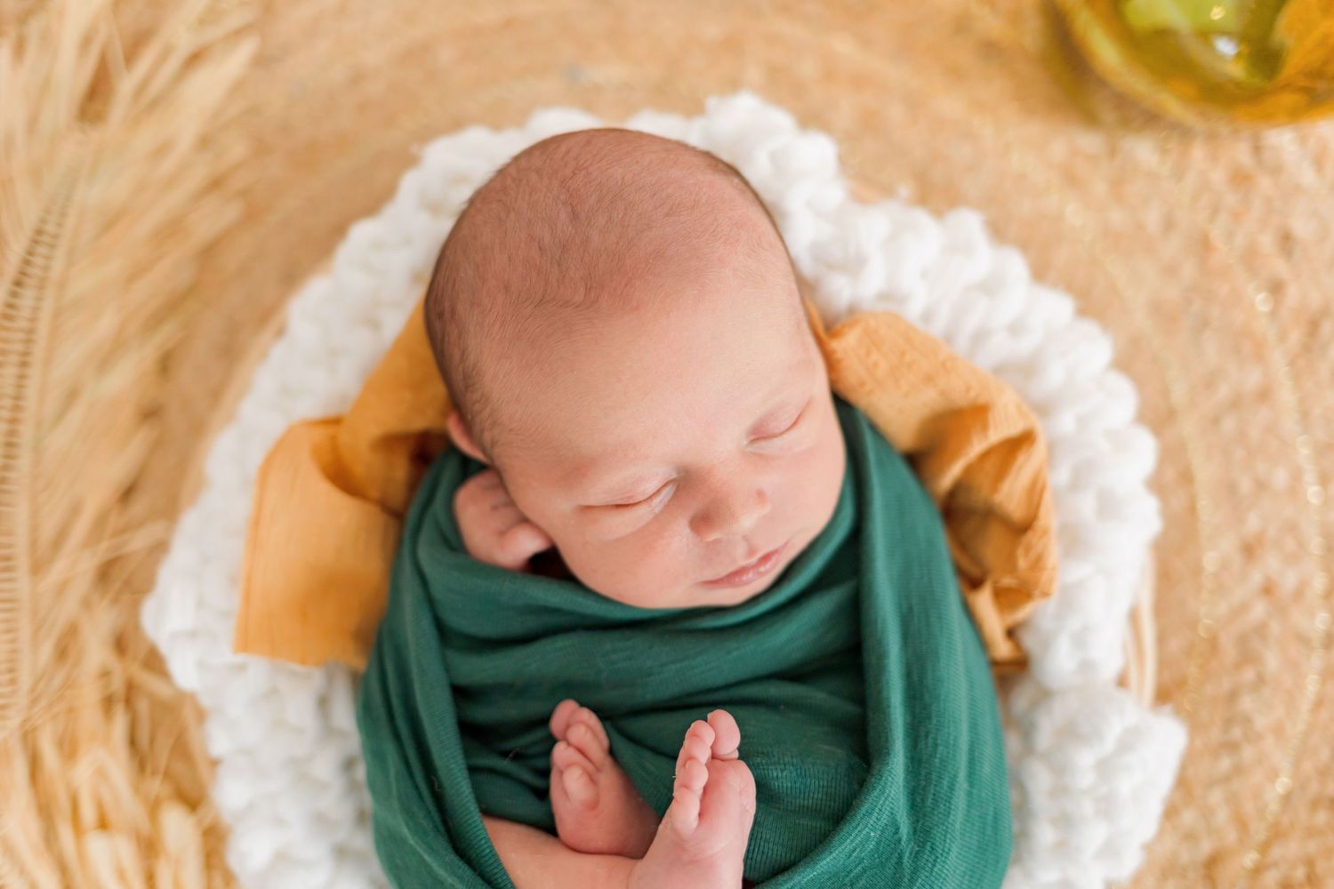 Close-up of sleeping newborn wrapped in forest green and gold swaddle on white cushioning.