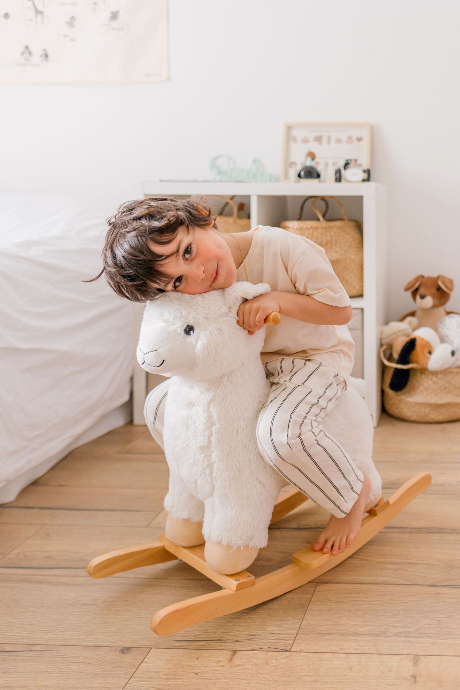 Child playing on a white rocking horse toy on wooden flooring in a minimalist room.