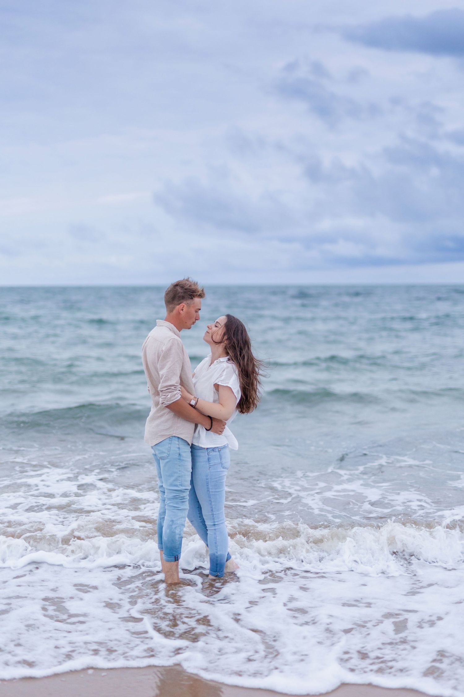 A romantic embrace captured on the beach with waves rolling in at their feet.