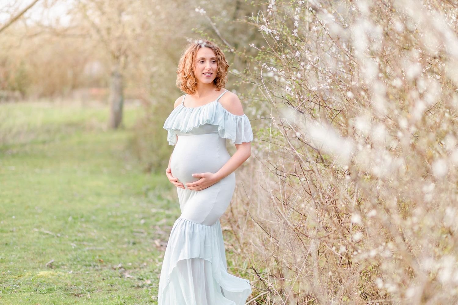 Expectant mother in flowing blue dress poses elegantly in a spring garden setting.