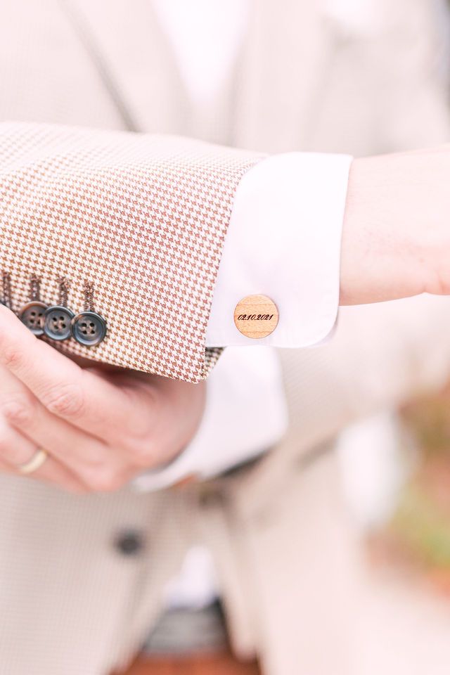 Close-up of beige checkered suit sleeve with white cuff and wooden button detail.