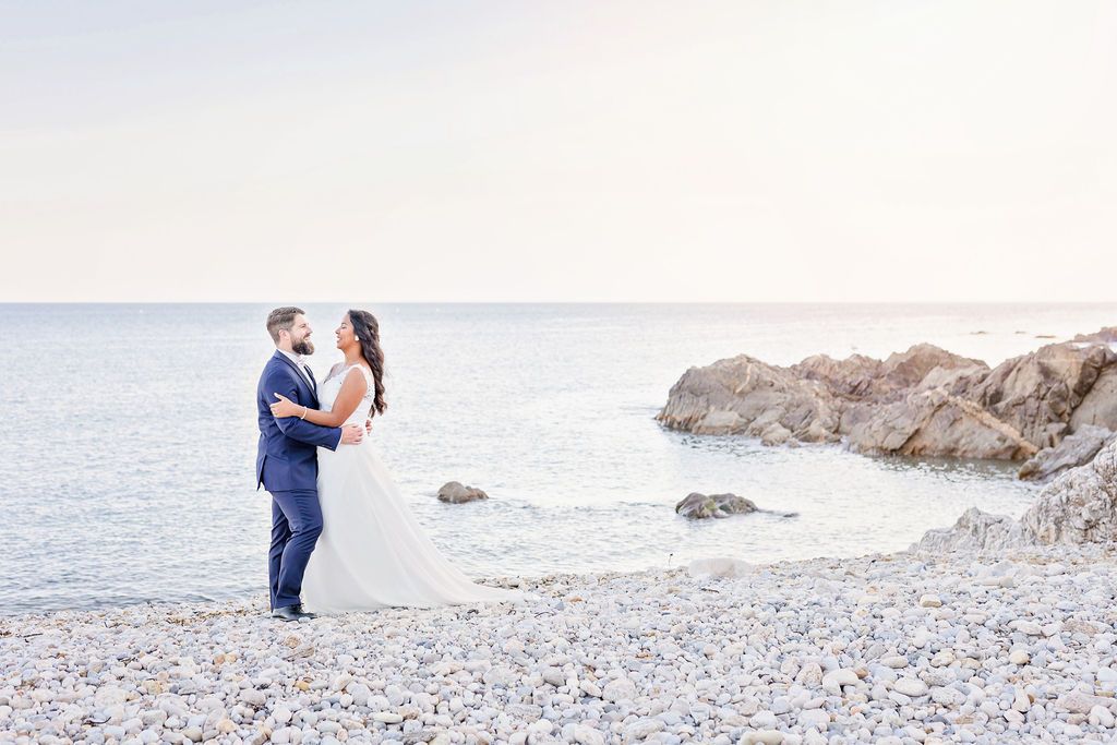 A serene coastal wedding photoshoot with couple against rocky shoreline in dreamy light.