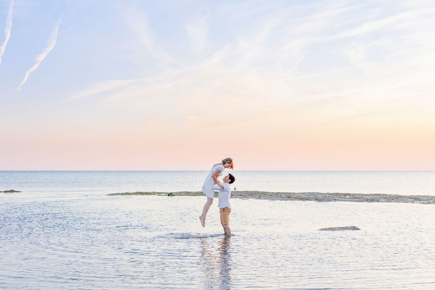 A couple enjoys an intimate moment together while standing in shallow beach waters at sunset.