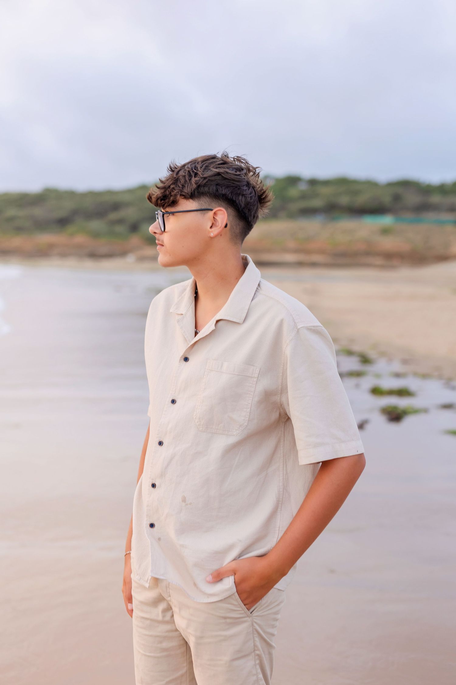 A person in a white button-down shirt and khaki shorts poses on a beach.