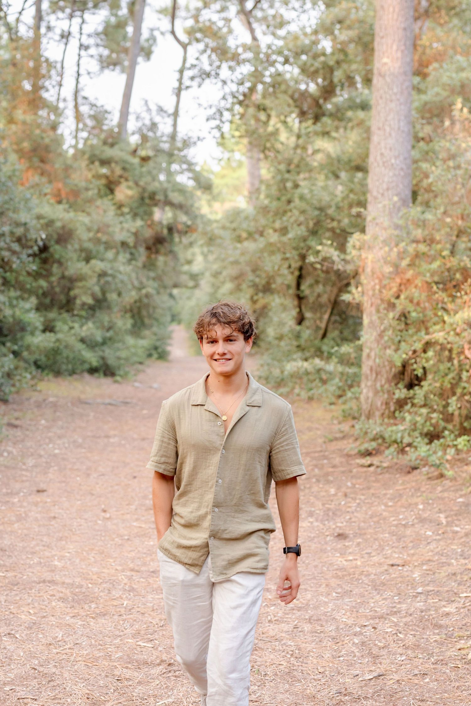 Young person in beige shirt and white pants walking casually along a wooded path.