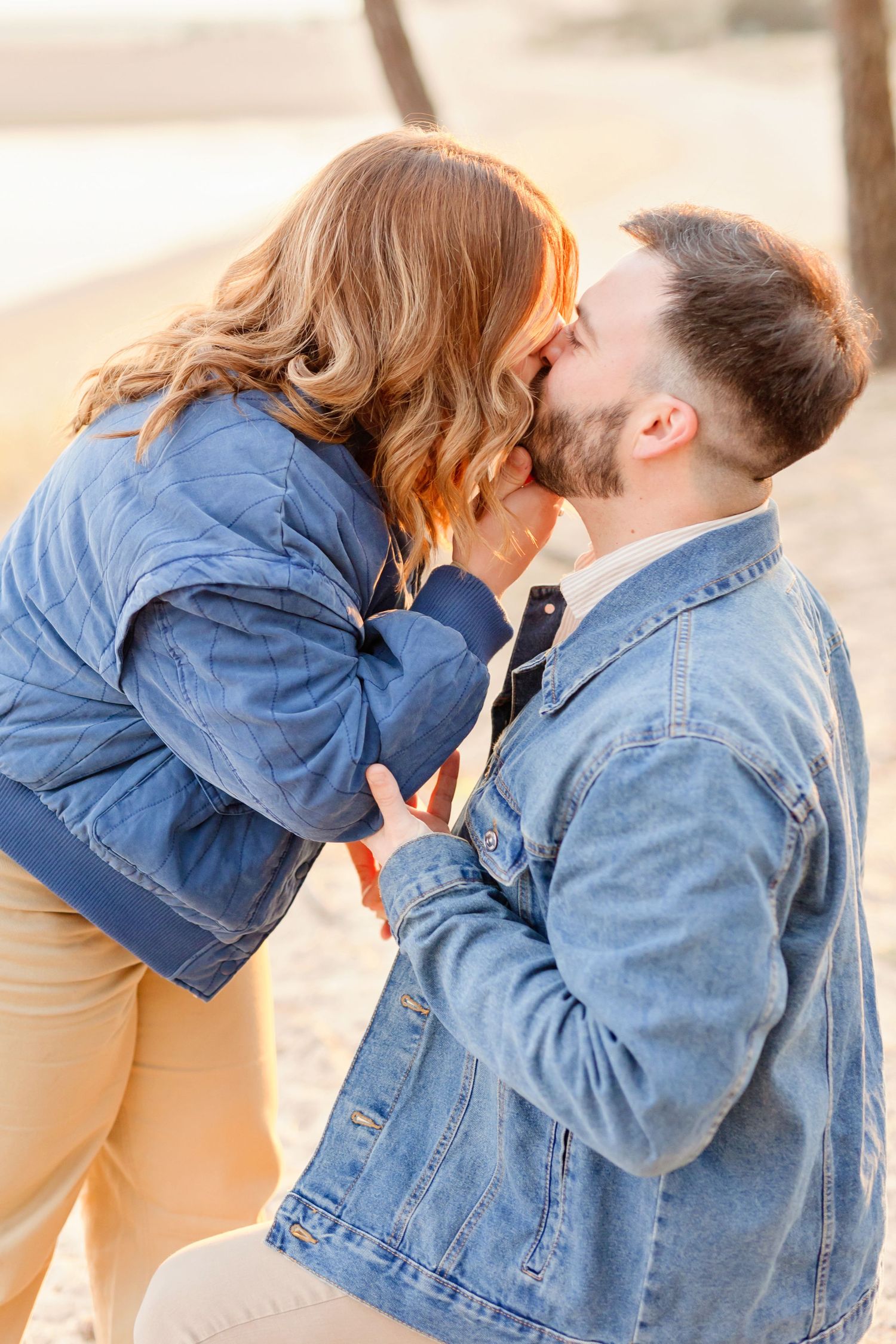 A romantic kiss shared between two people in matching denim jackets at sunset.