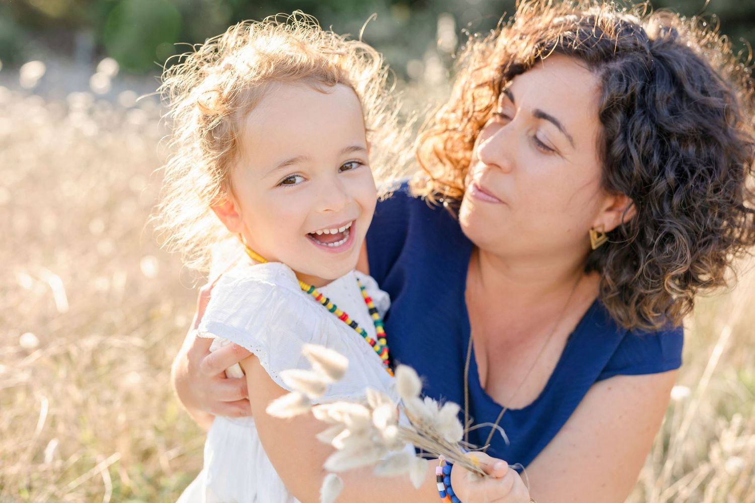 Parent and child sharing laughter while playing in tall grass.
