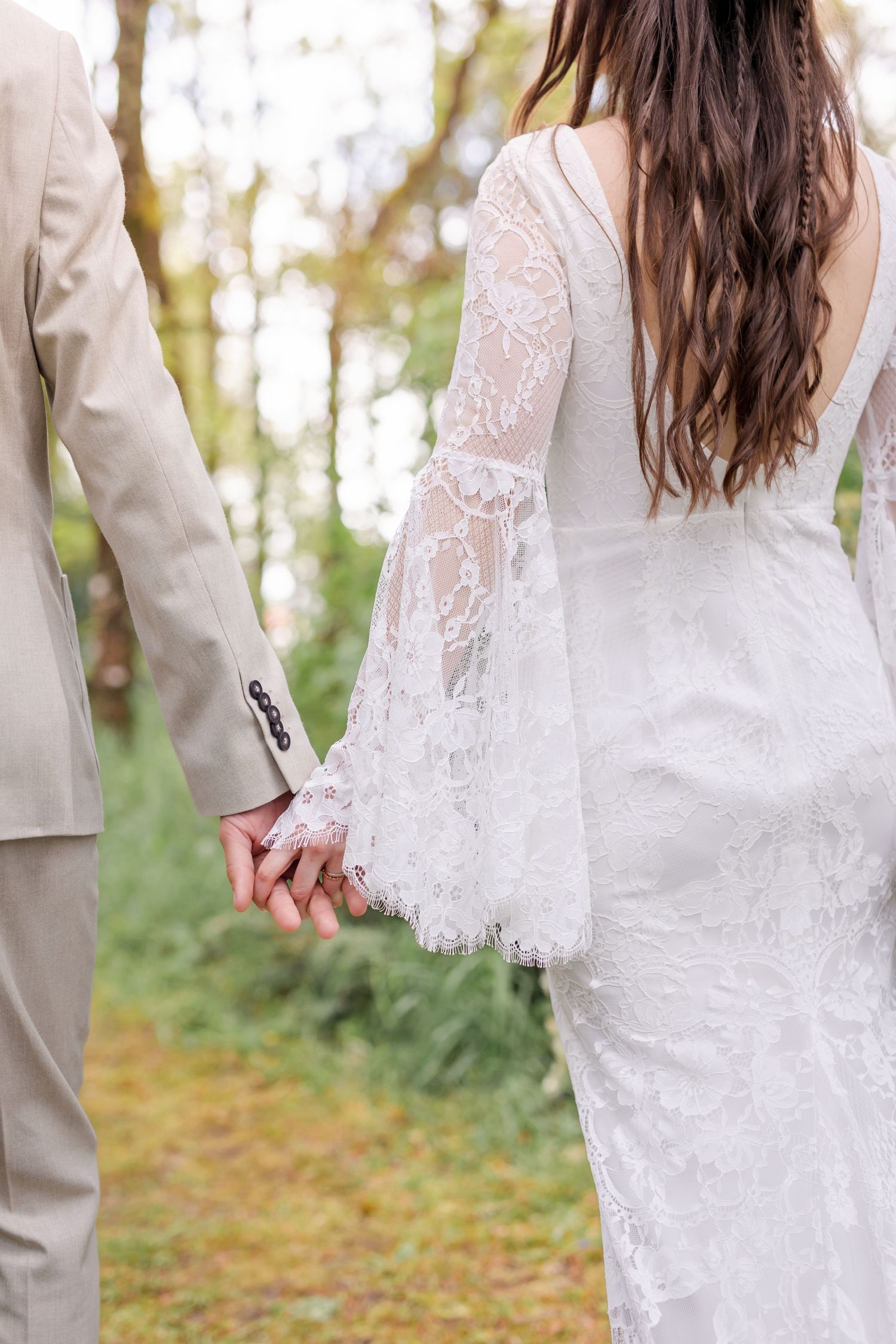 Detail shot of a bride's lace sleeve wedding dress and couple holding hands.