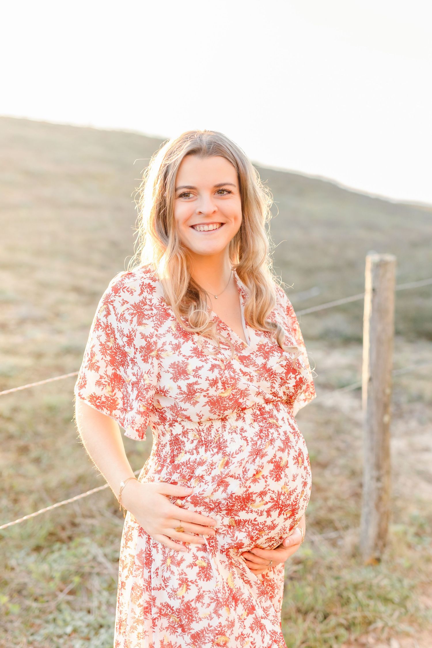 A woman in a floral dress standing in a field during golden hour.