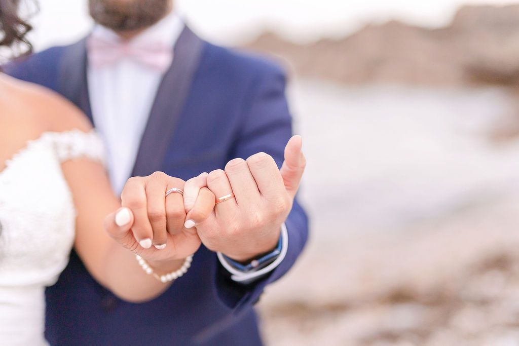 Wedding ring detail photo showing hands joining together on a sandy beach.