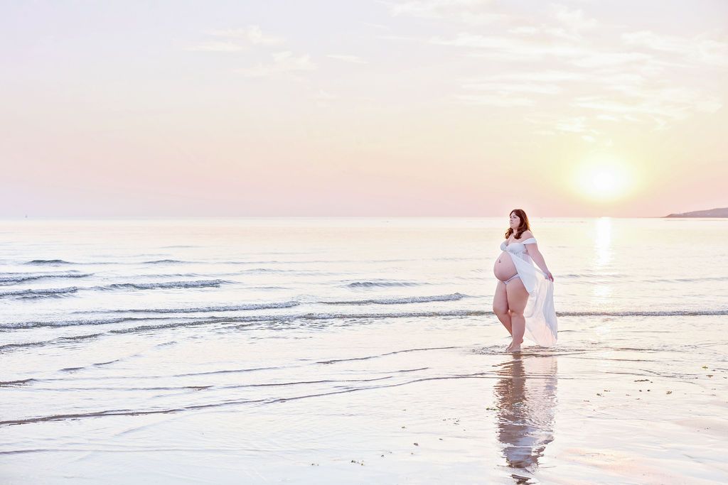 Ethereal beach scene with person in white dress walking near ocean waves at sunset.