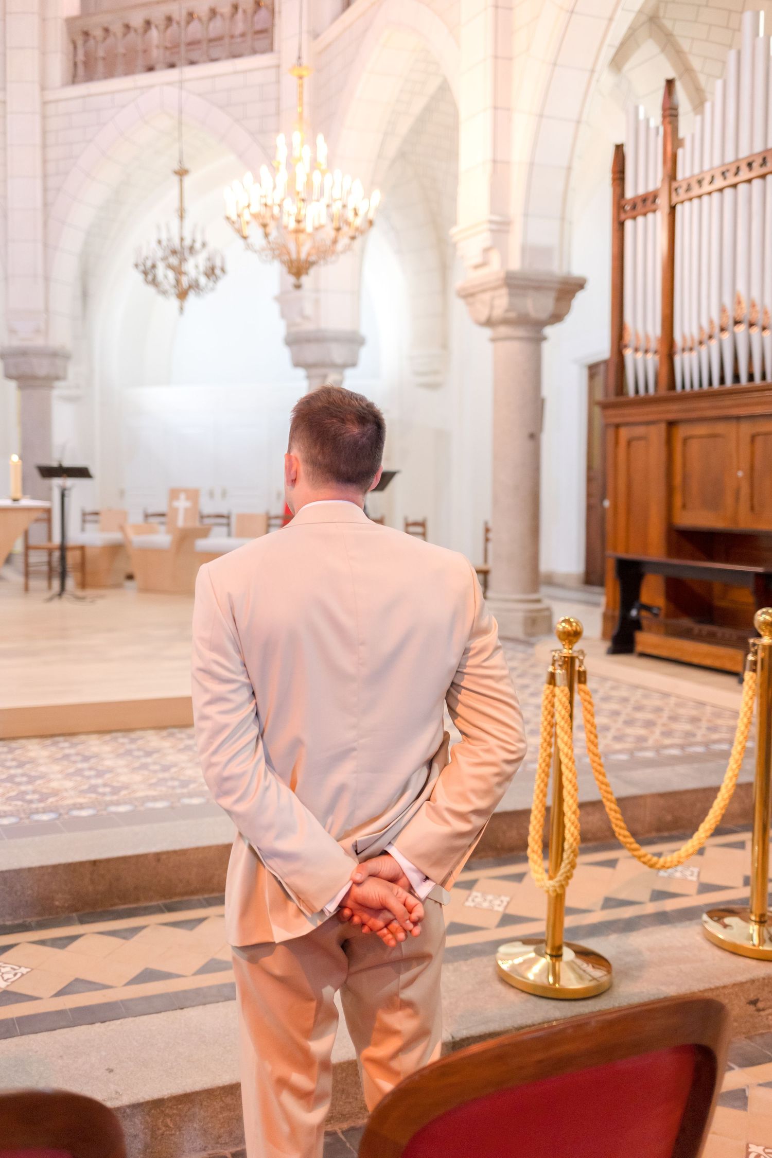 A groom stands with clasped hands in a church sanctuary facing the altar.