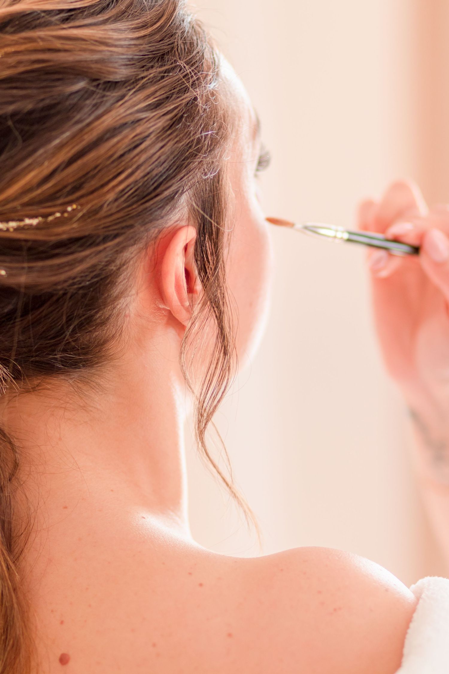 Close-up shot of applying makeup with a brush to someone's ear area during wedding preparations.