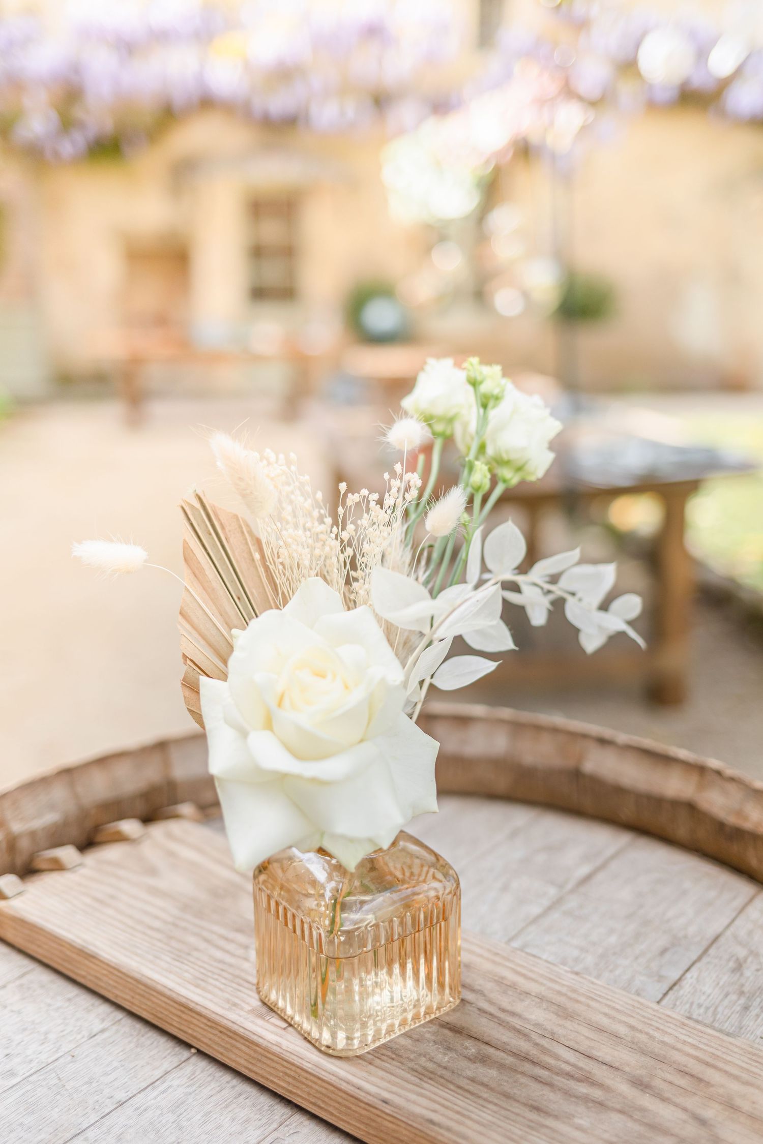 Elegant white rose centerpiece arrangement in a gold-rimmed glass vase on weathered wood surface.