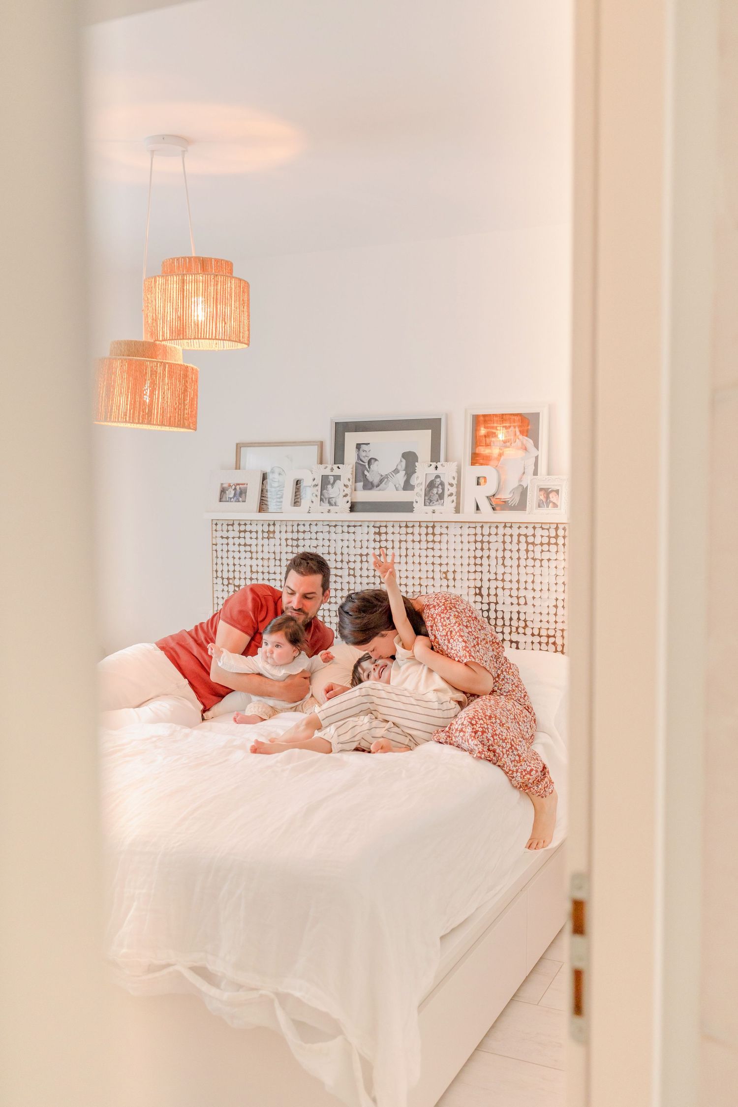Family members sharing joyful moments together while lounging on white bedding in a bright sunlit room.
