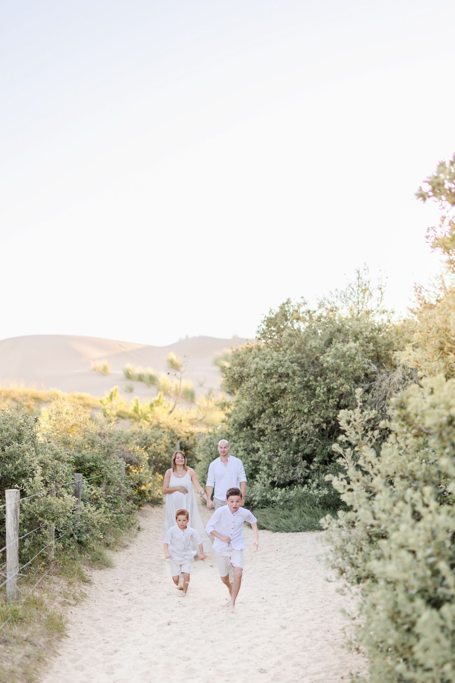 Group dressed in white walking along sandy path surrounded by coastal vegetation.