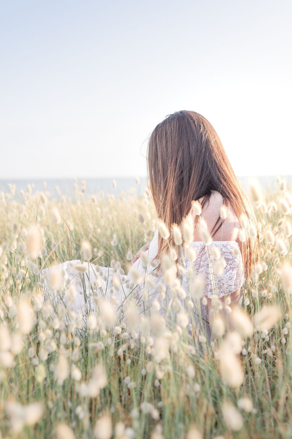 A figure sits among delicate white wildflowers in a dreamy meadow during golden hour.
