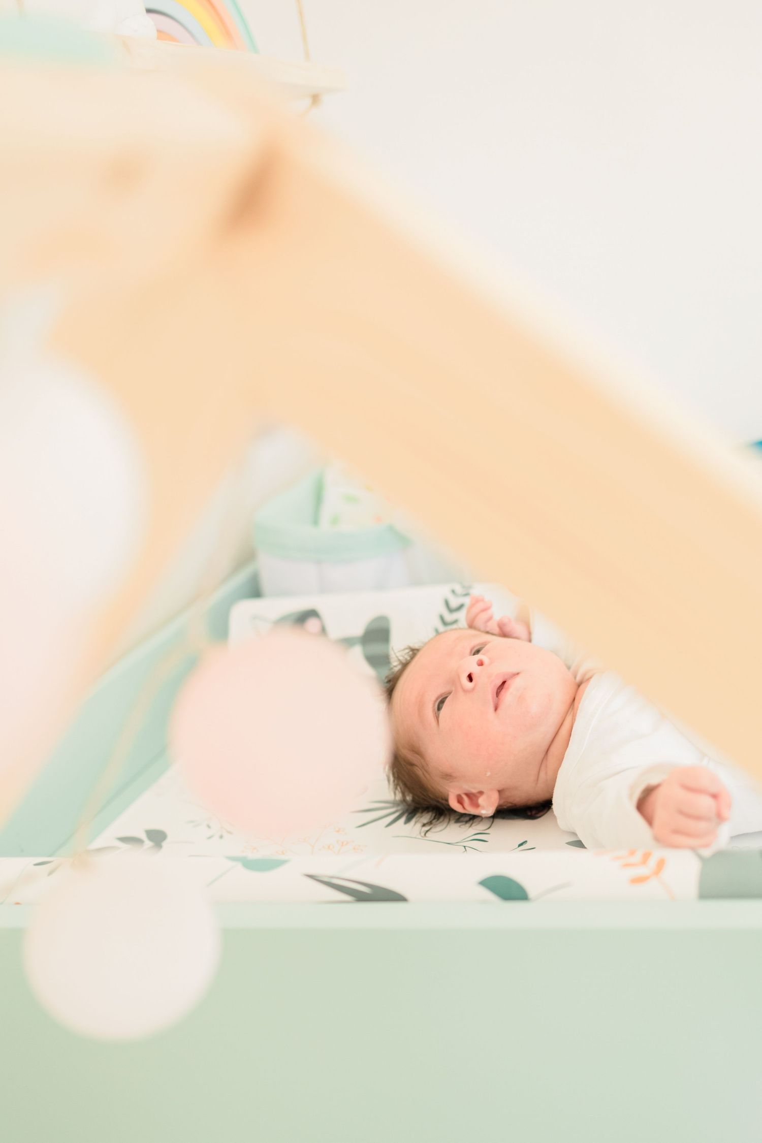 Overhead view of baby lying on mint green changing pad with soft bokeh effect.