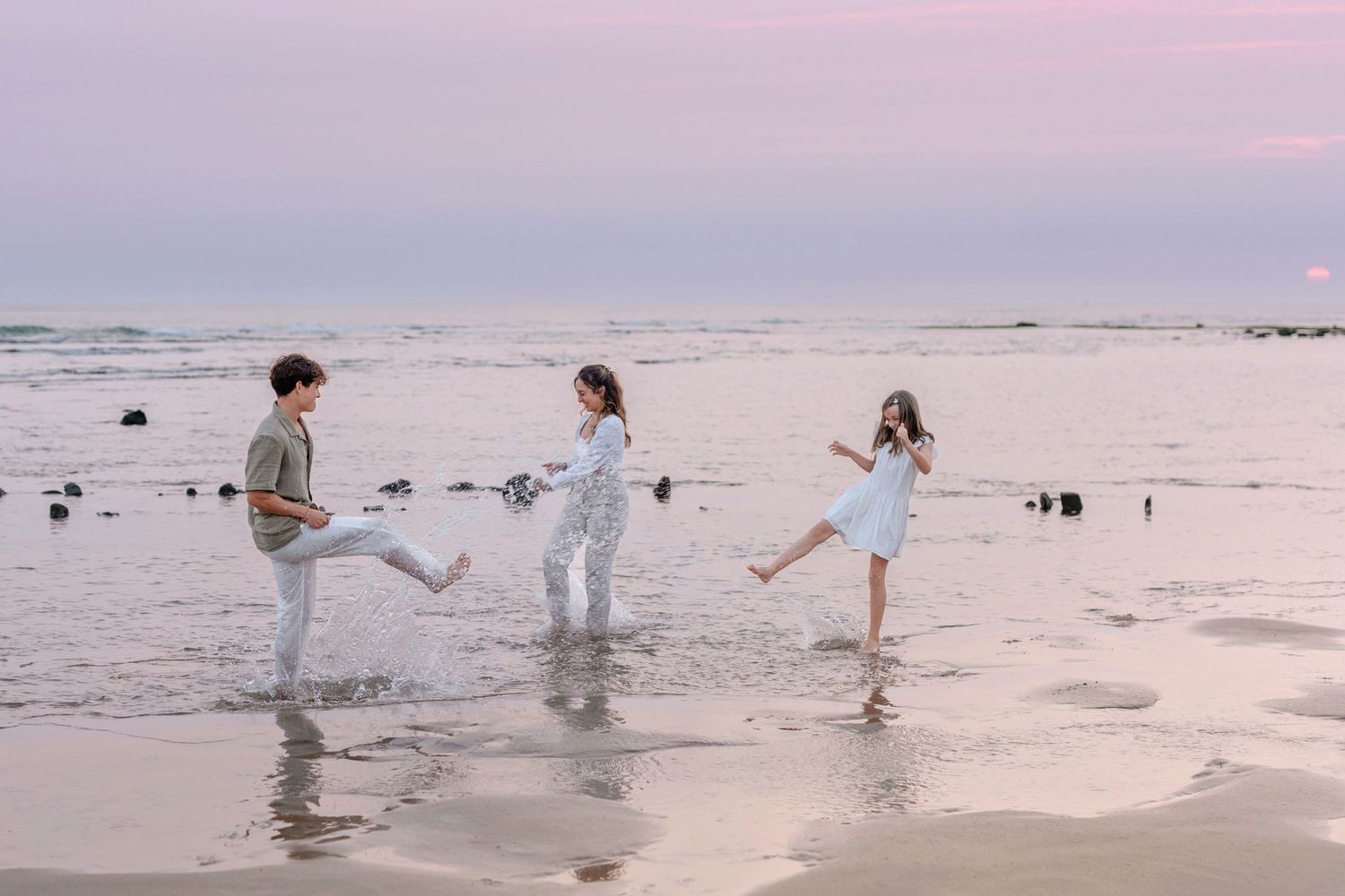 People playing and kicking water on beach at dusk.