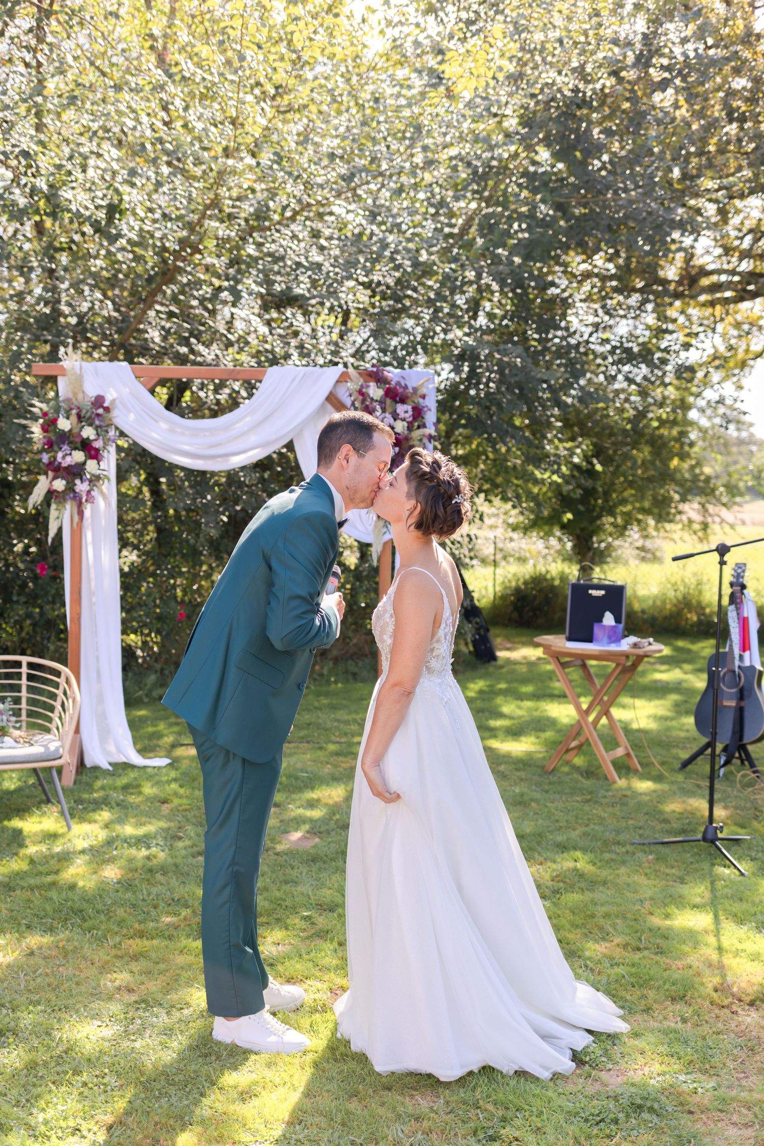 A romantic outdoor wedding ceremony under trees with white drapery and sunlit backdrop.