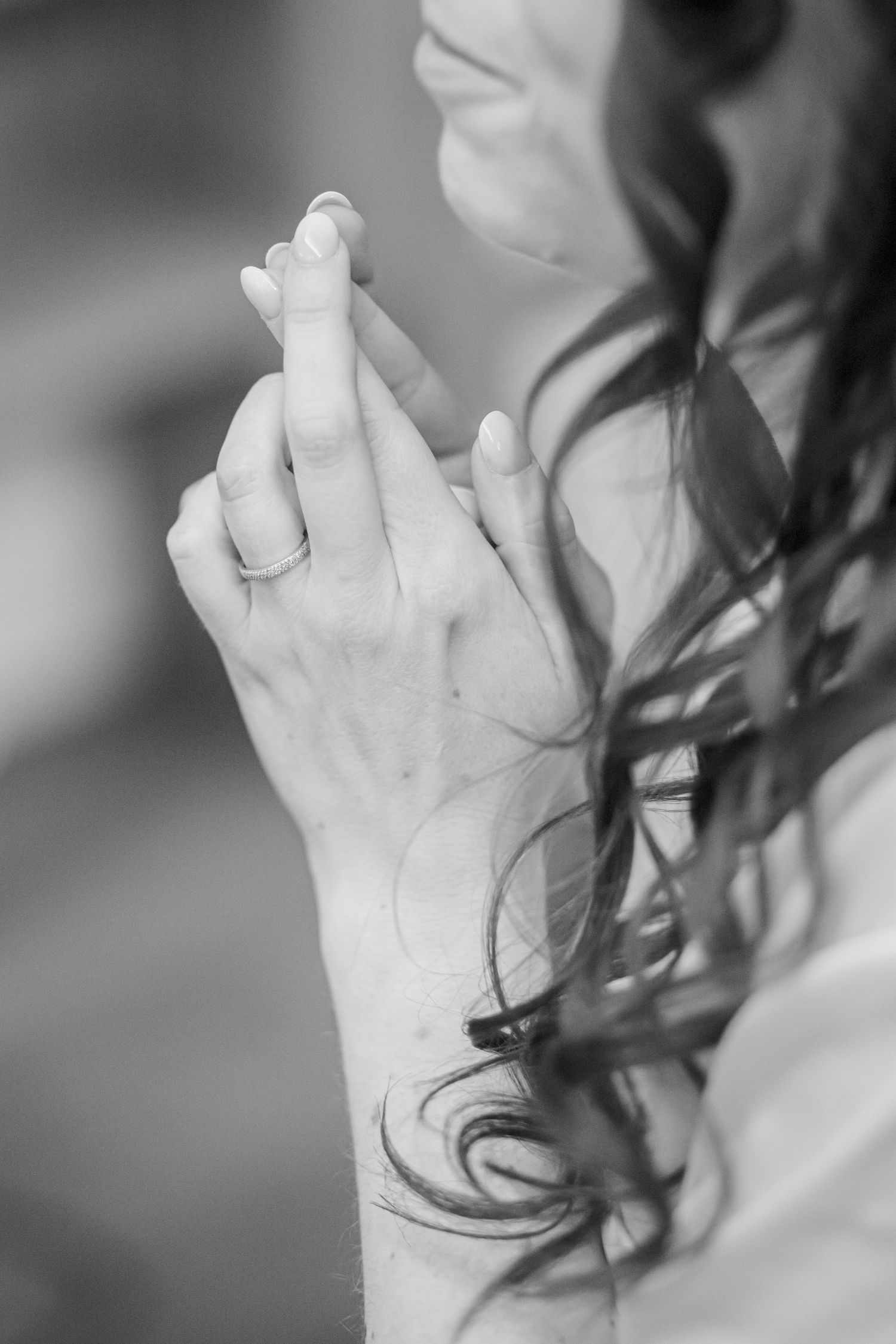 Black and white close-up of hands with rings and curled hair.