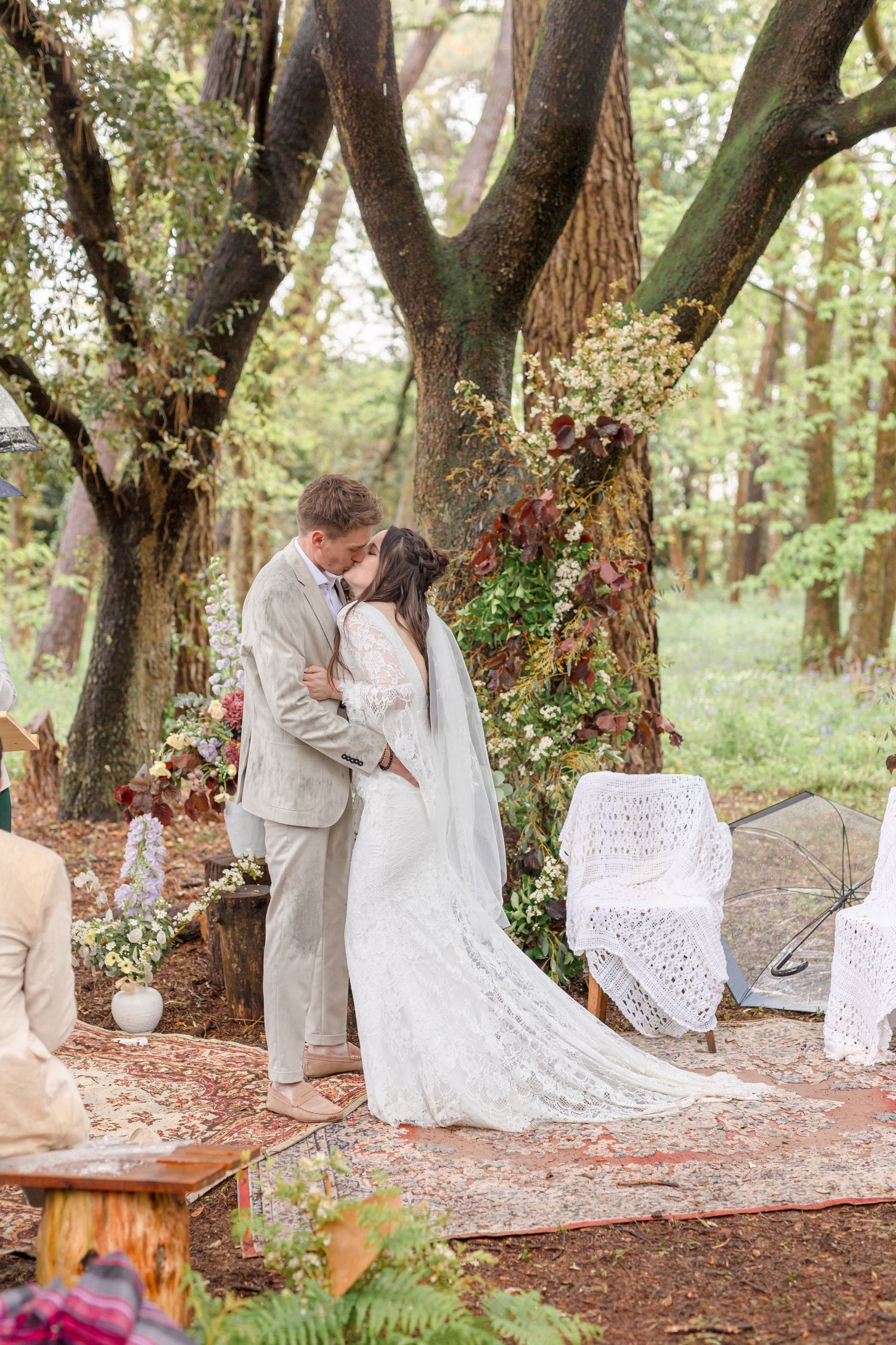 Newlyweds share their first kiss at a rustic woodland wedding ceremony with decorative details.
