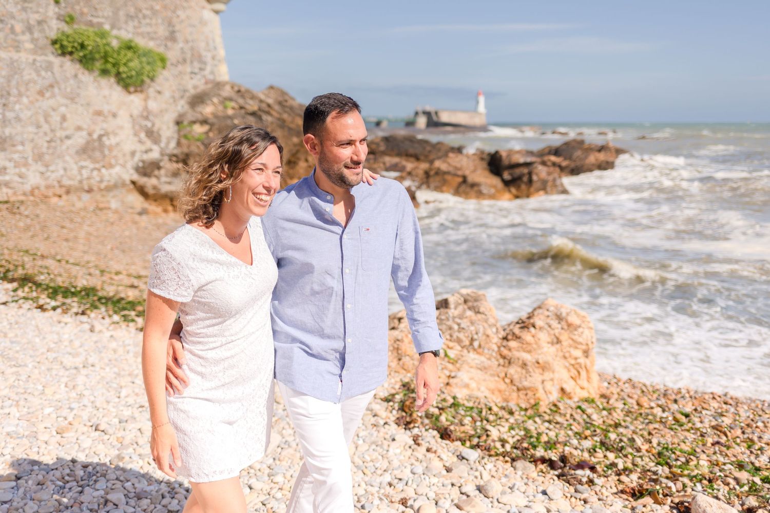 Romantic stroll along scenic coastal path with lighthouse and rocky shore in background.