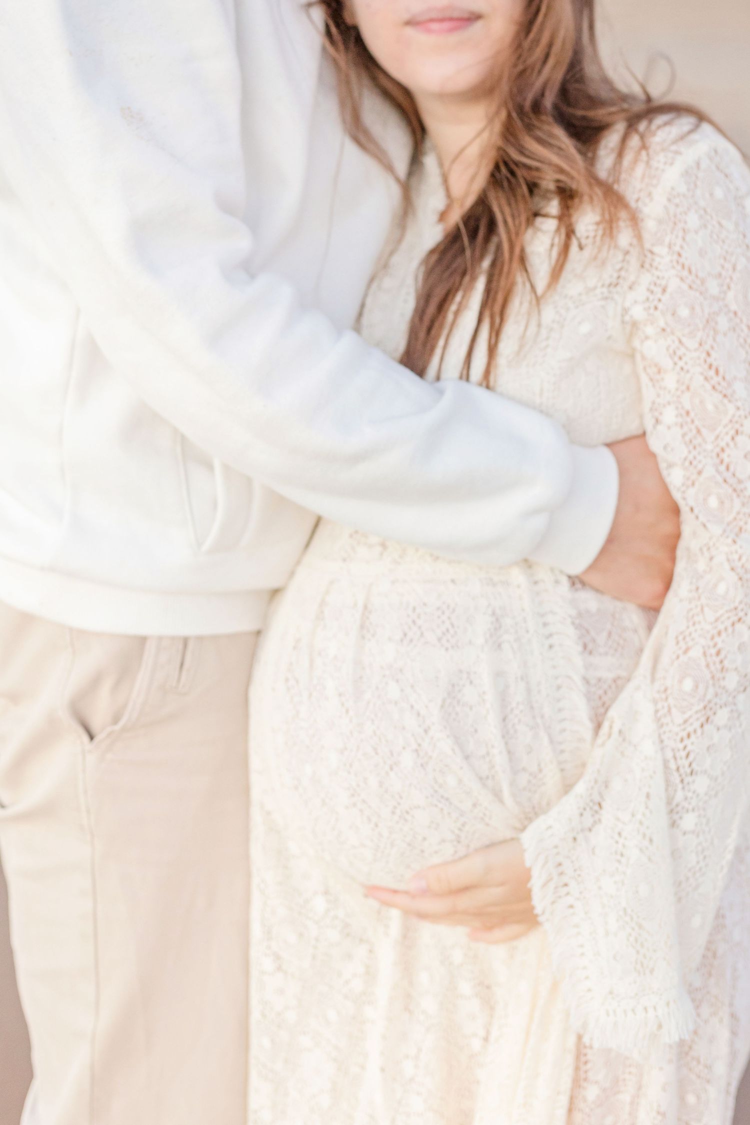 Intimate maternity photo showing white lace dress details and gentle hand placement.